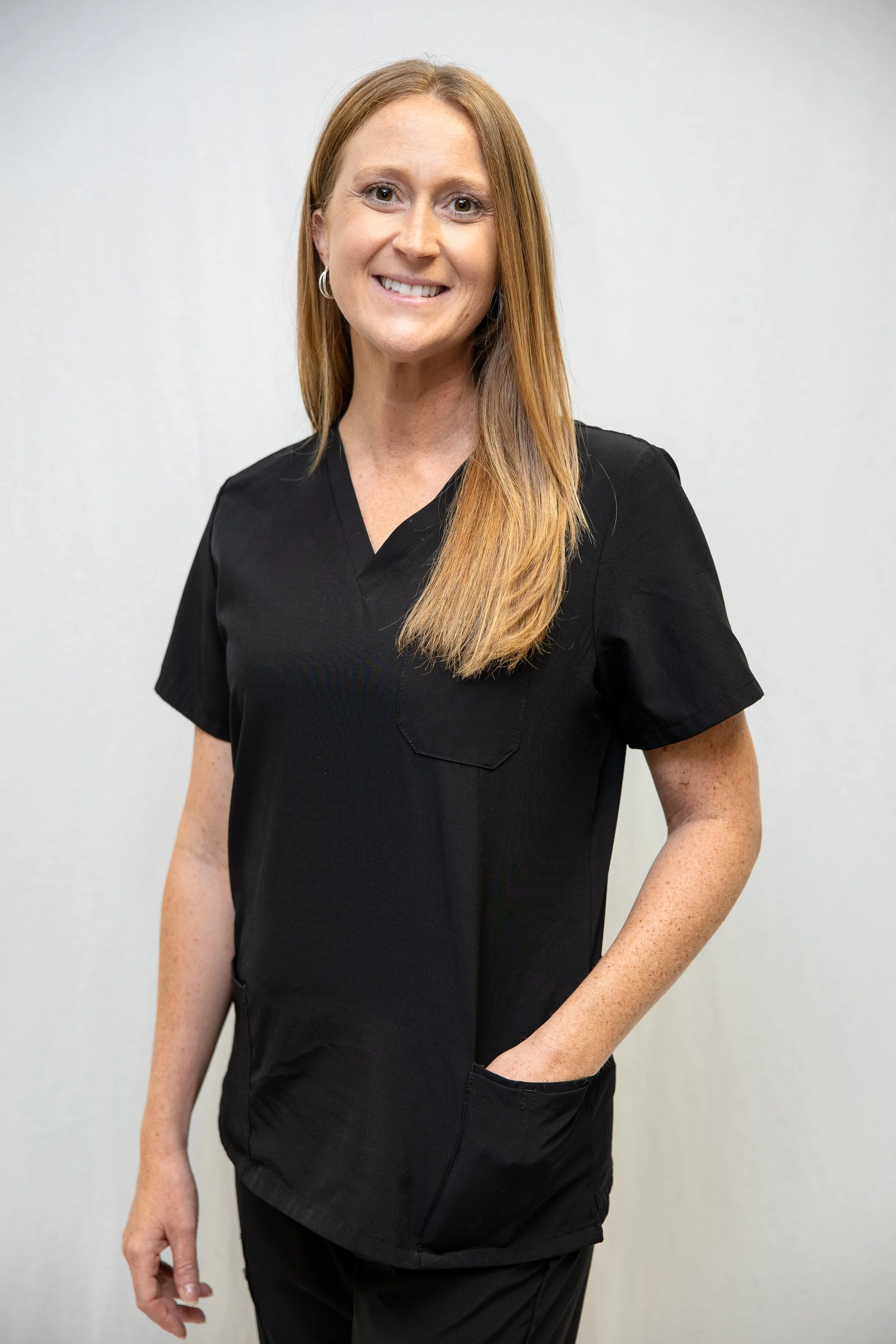 A smiling woman in a black medical uniform standing against a plain white wall.