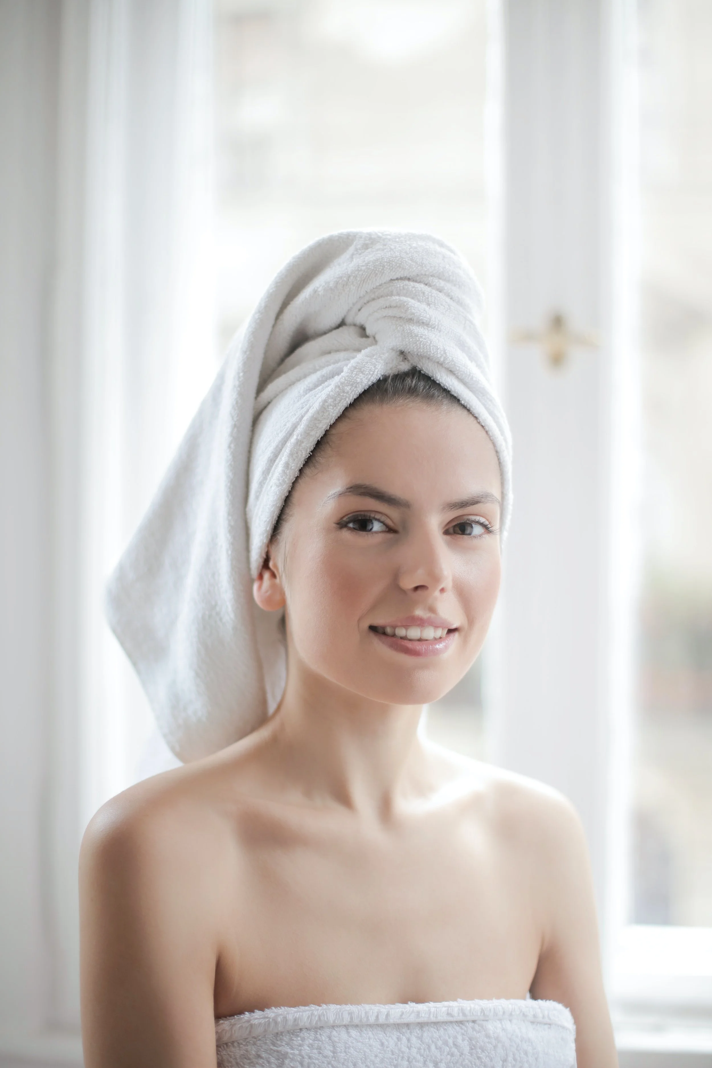 A woman with a towel wrapped around her head, smiling at the camera in a bright room.