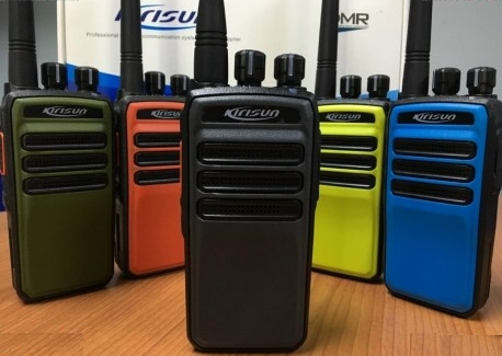 Five handheld walkie-talkies in black, yellow, blue, orange, and green colors, placed on a wooden surface.