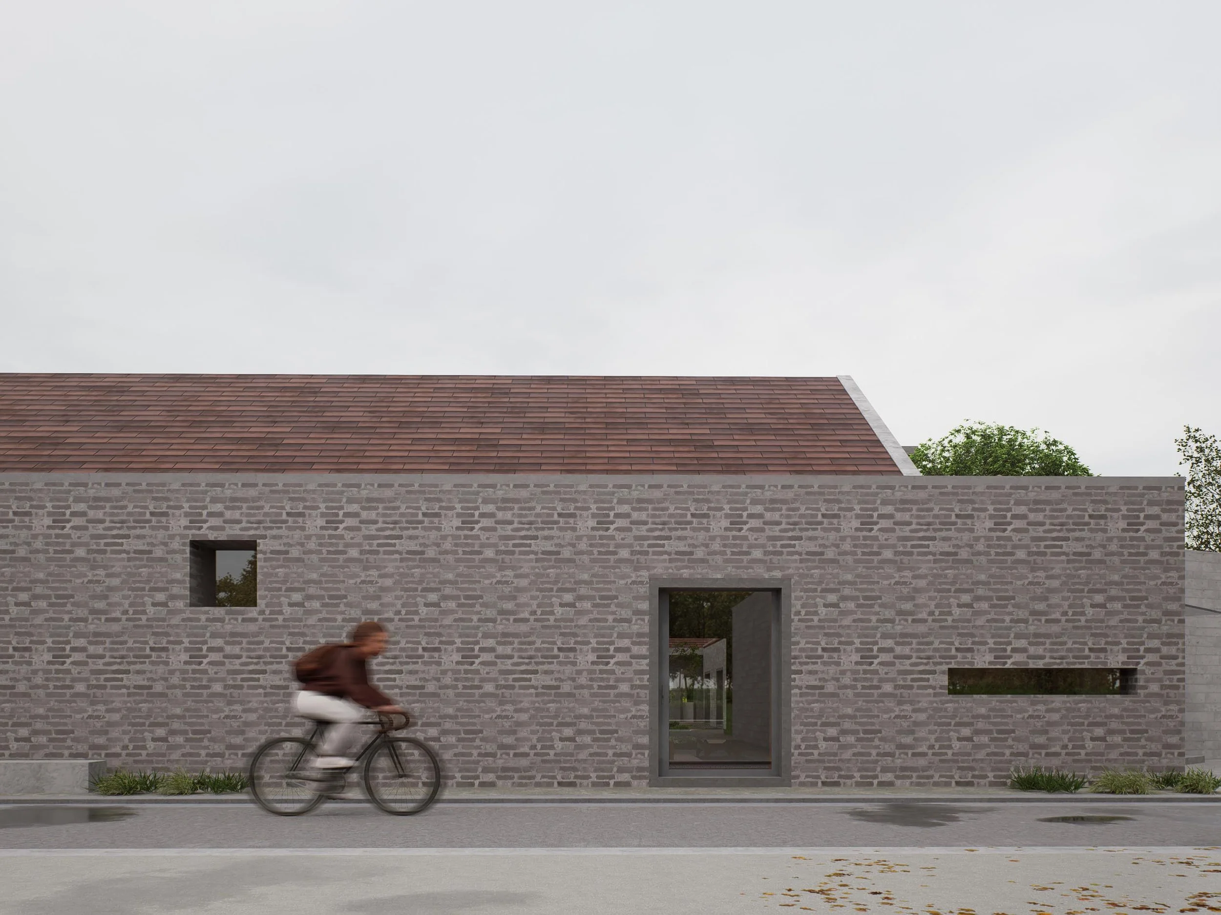 A person biking past a modern brick building with small rectangular windows under an overcast sky.