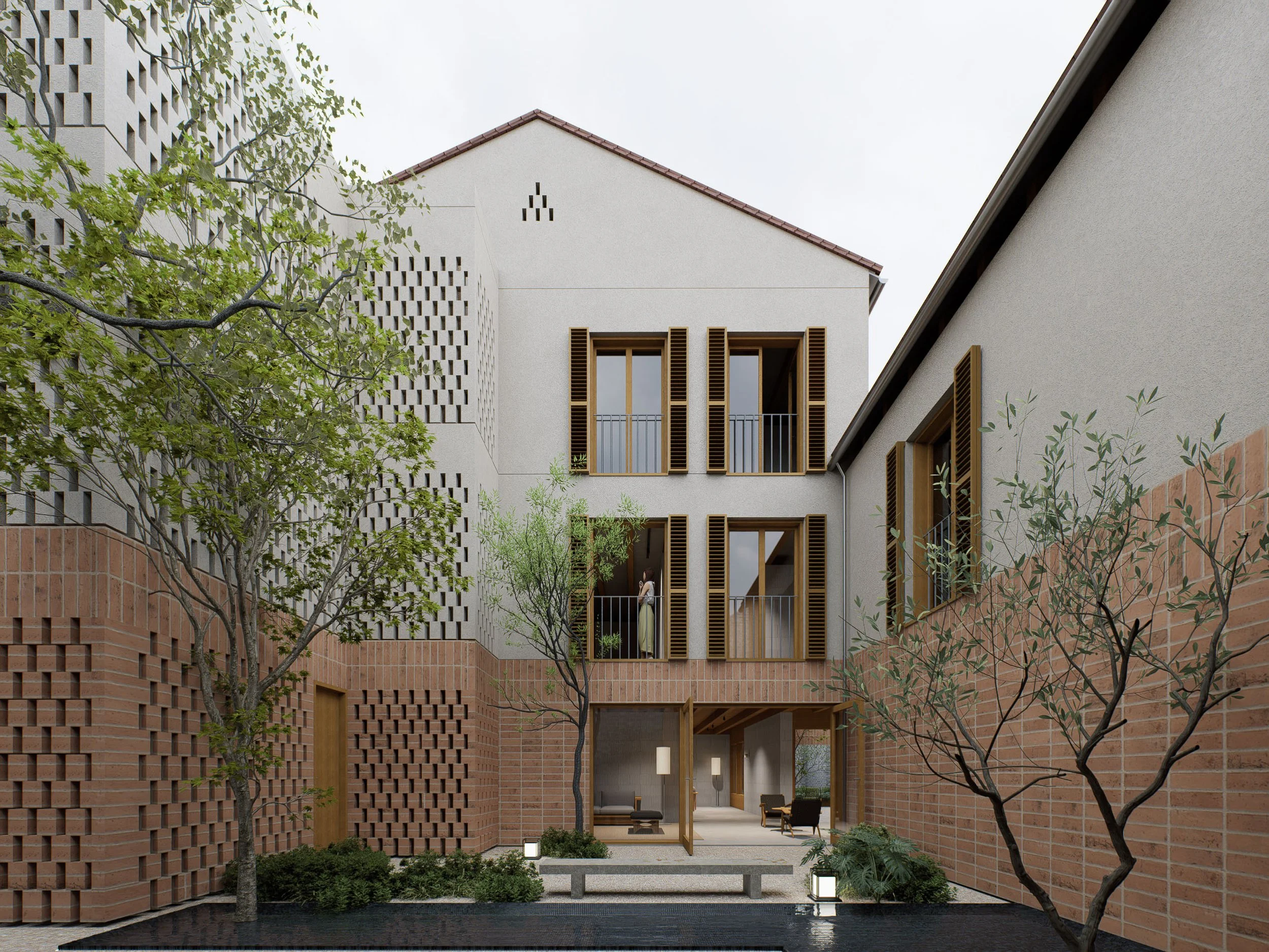 A modern, multi-story residential building with exposed brick and wood accents, open balconies with glass railings, and large windows with wooden shutters. The courtyard has trees, benches, shrubbery, and outdoor lighting, with a woman standing on one of the balconies.