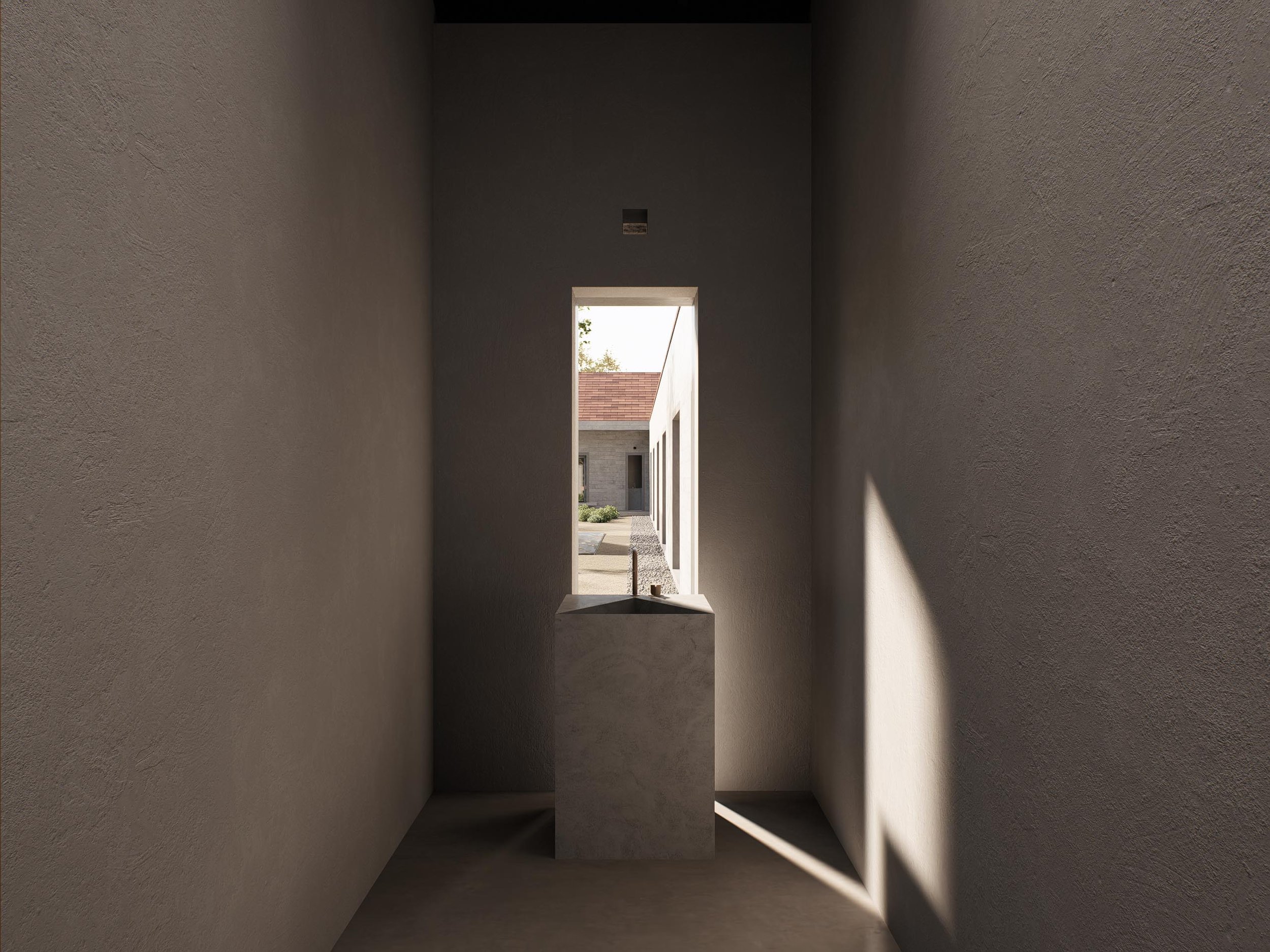Interior view of a minimalist room with textured walls, a rectangular window with no glass, and a stone pedestal with a sink in front of it. Sunlight casts shadows on the right wall, revealing an outdoor scene with a building and trees.