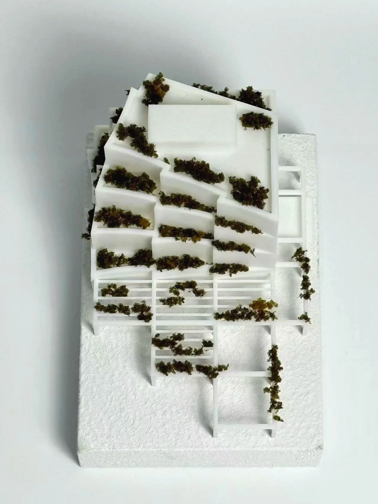 Architectural model of a modern, multi-level building with terraces and greenery, made of white foam and plastic.