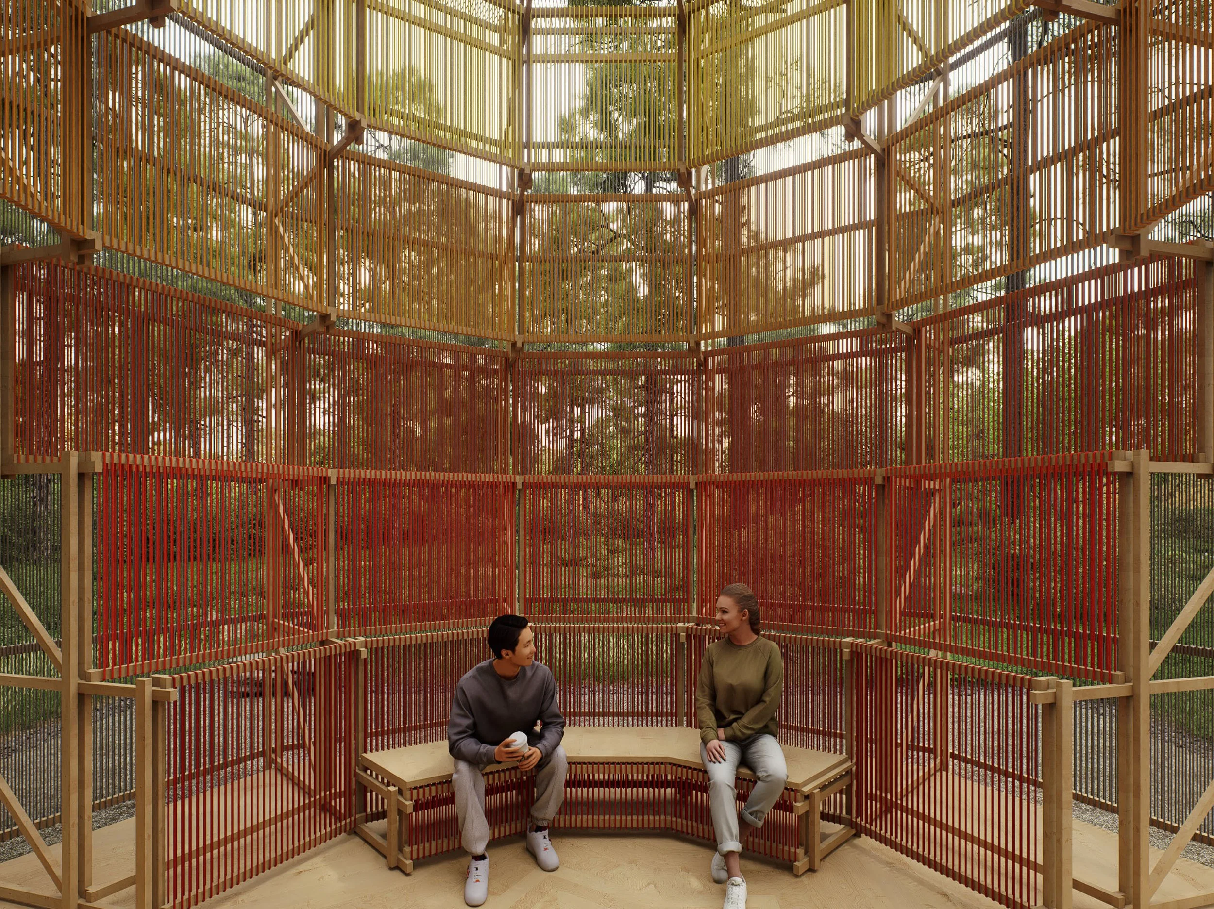 Two people sitting on a built-in wooden bench inside a treehouse with red and yellow vertical wooden slats forming the walls, surrounded by trees and greenery.