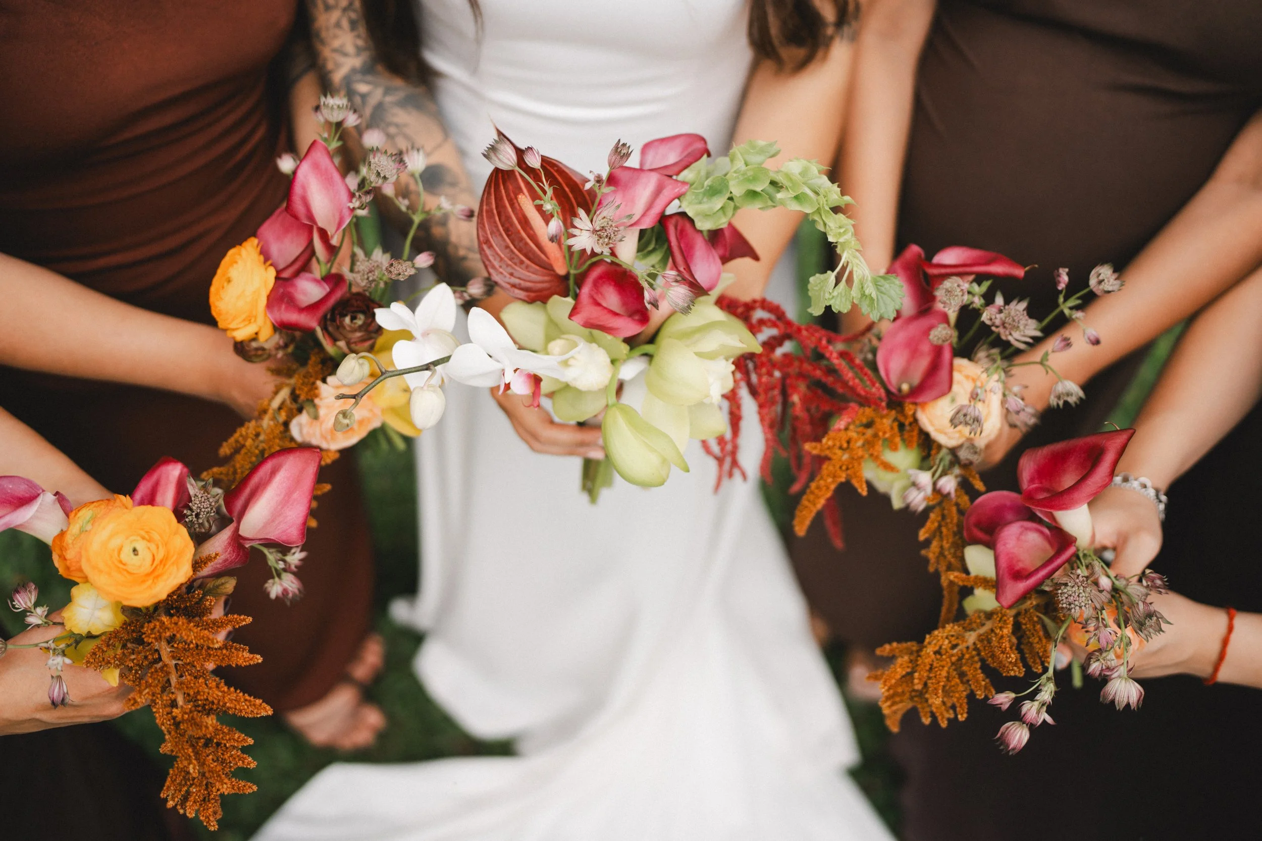People holding colorful flower bouquets, including calla lilies, orchids, and various other flowers, during a wedding or celebration.