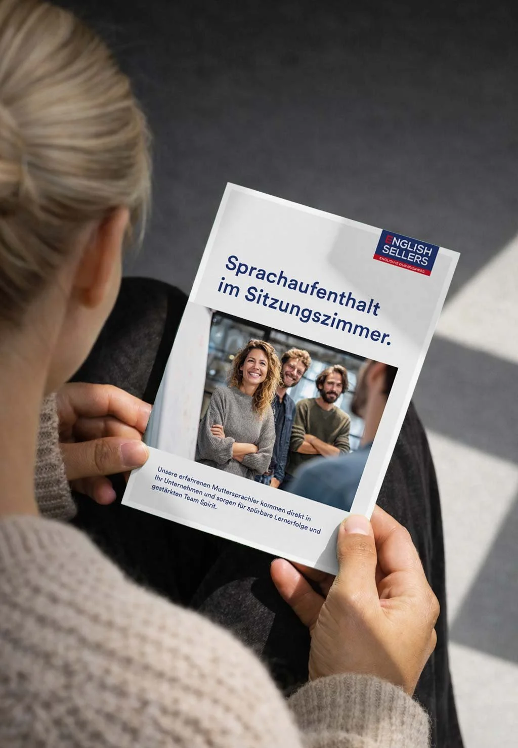 Flyer von English Sellers mit der Headline «Sprachaufenthalt im Sitzungszimmer.» in den Händen einer Person.