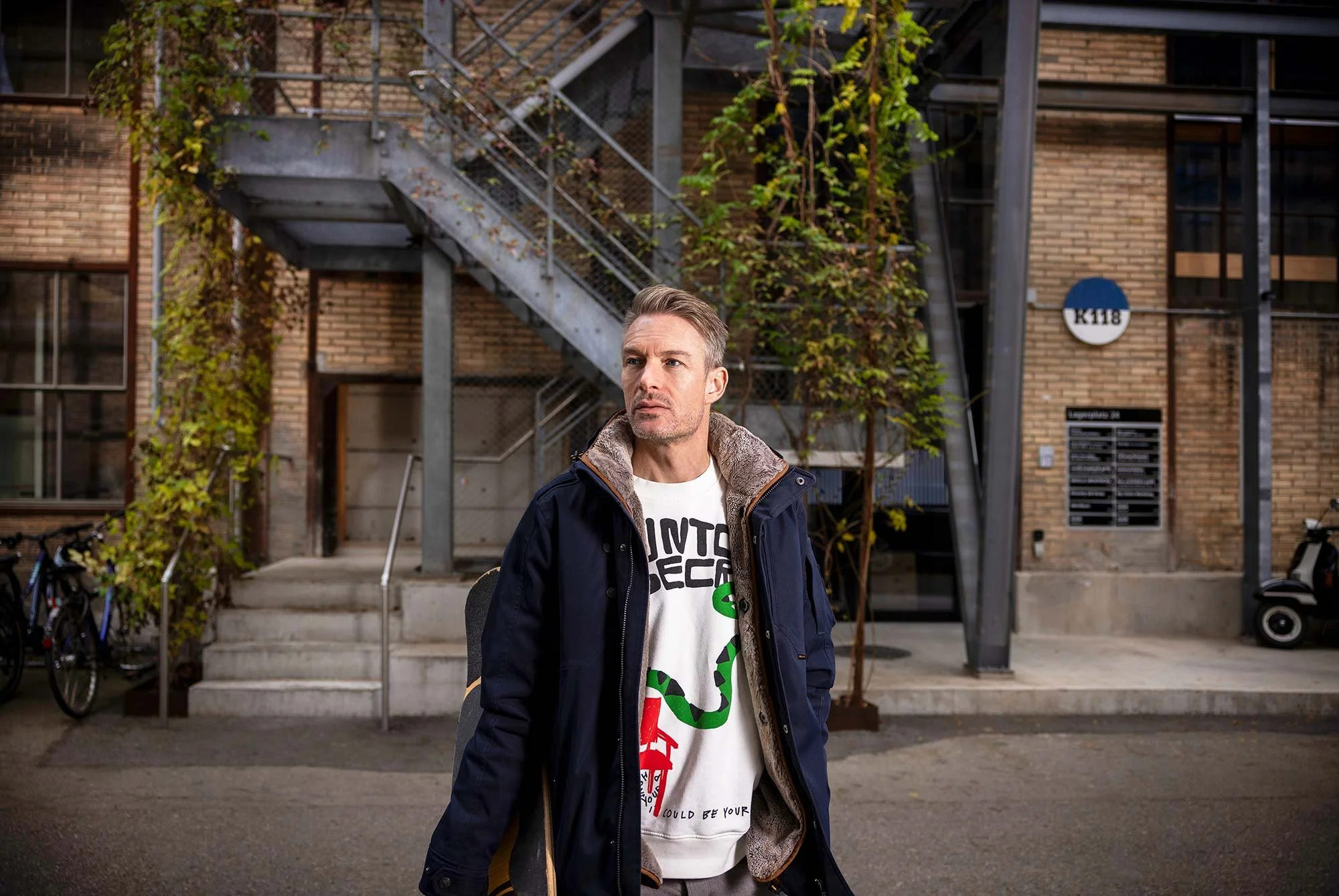 Sascha Völki mit Longboard und Winterjacke vor dem Upcycling-Gebäude.