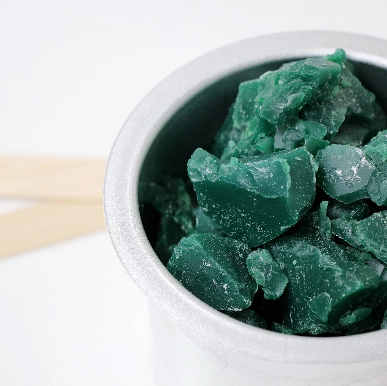 Green crystalline chunks in a metal container on a white surface.