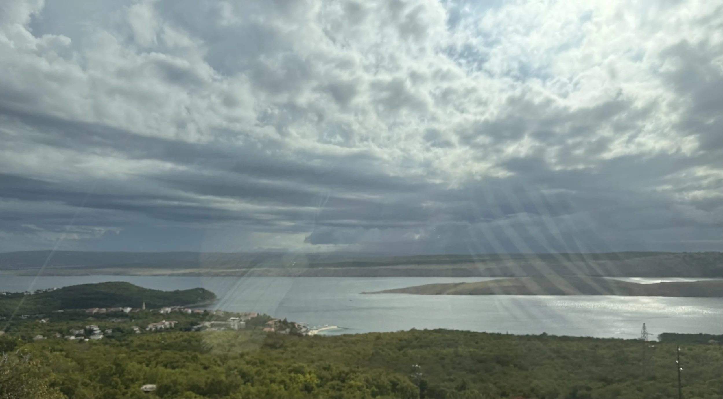 Scenic view of a river or lake with surrounding greenery and hills under a cloudy sky.