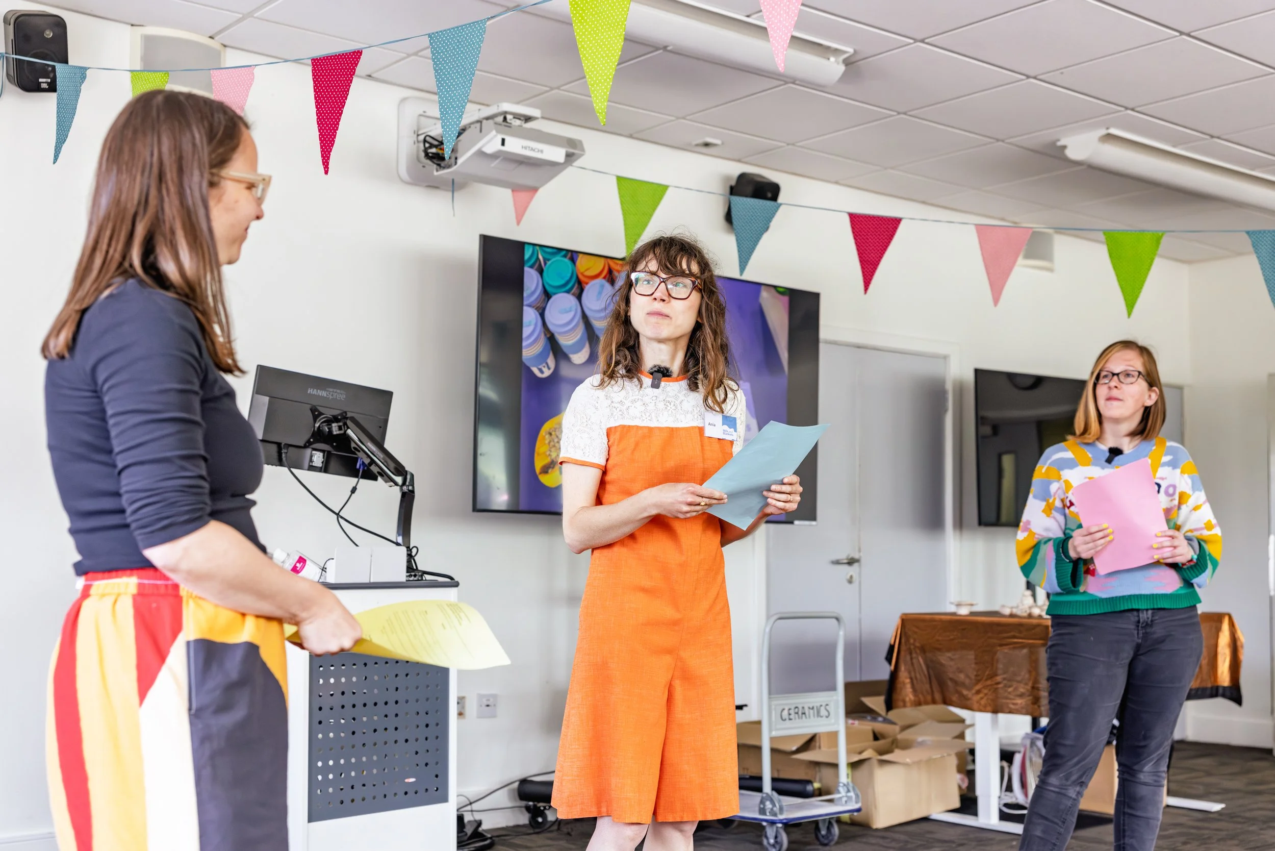 Three women standing in a room, reading from scripts in their hands.