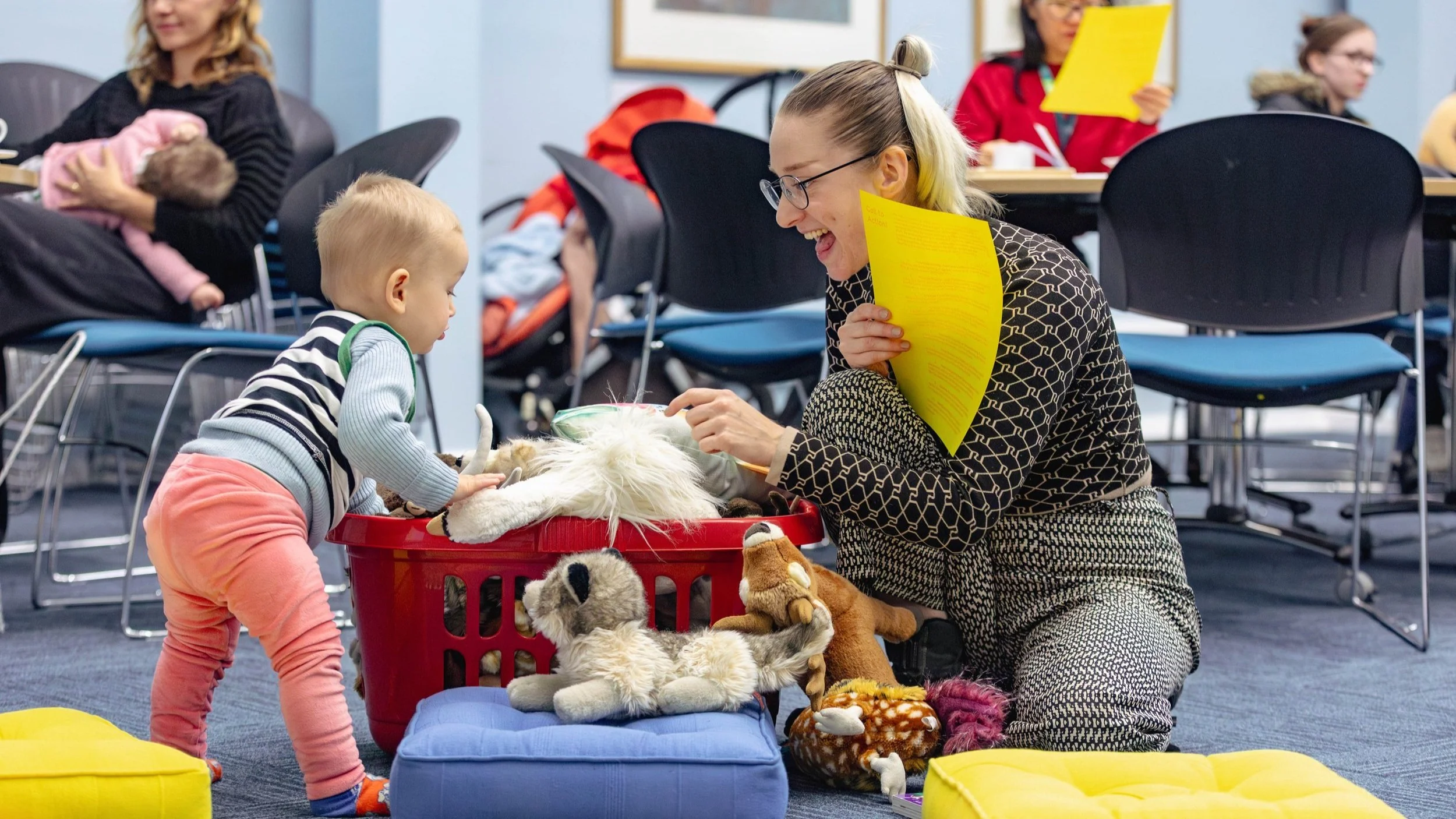 A woman and toddler sitting on a floor next to a basket of toys.