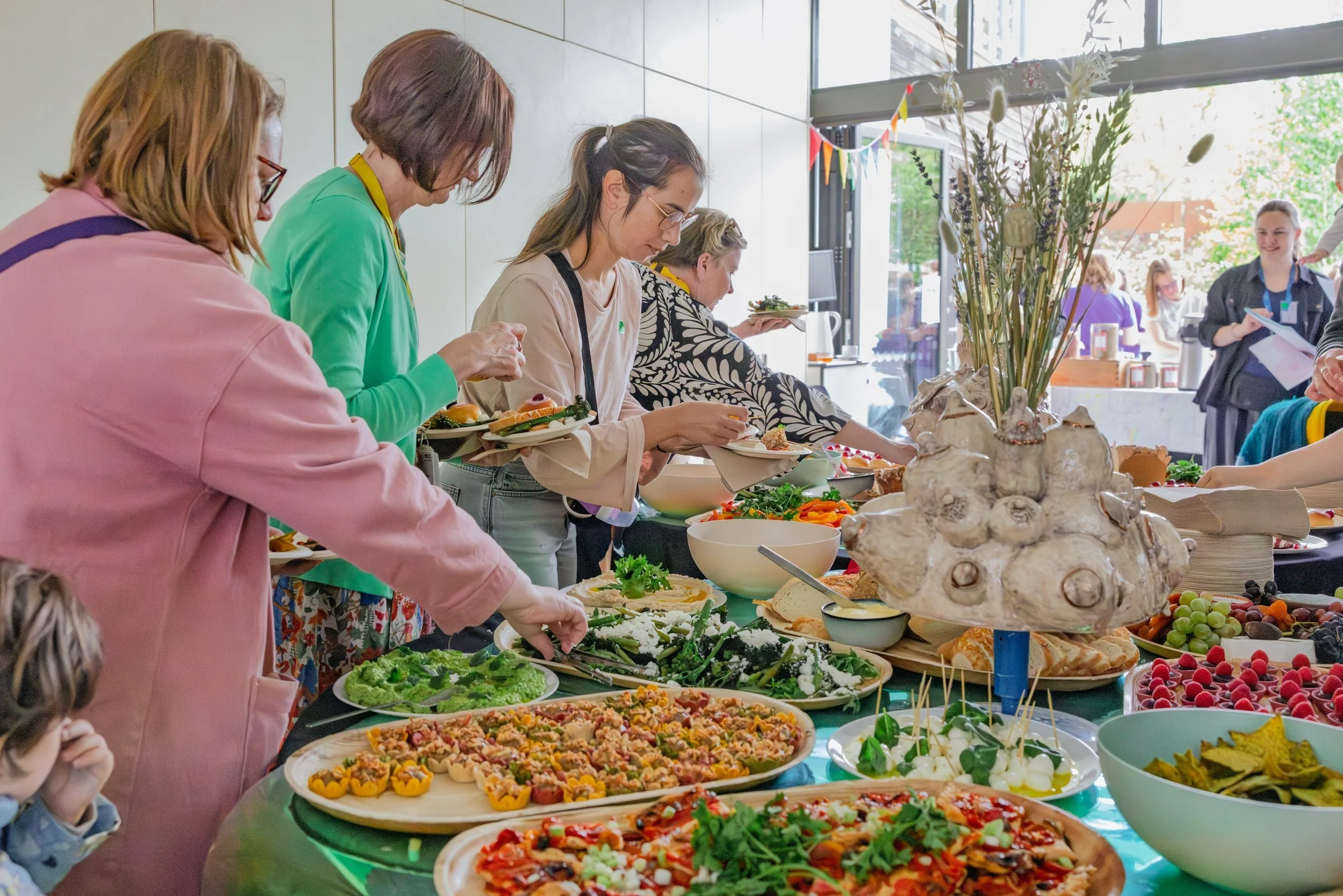 People serving themselves food from a buffet, with a ceramic centrepiece.