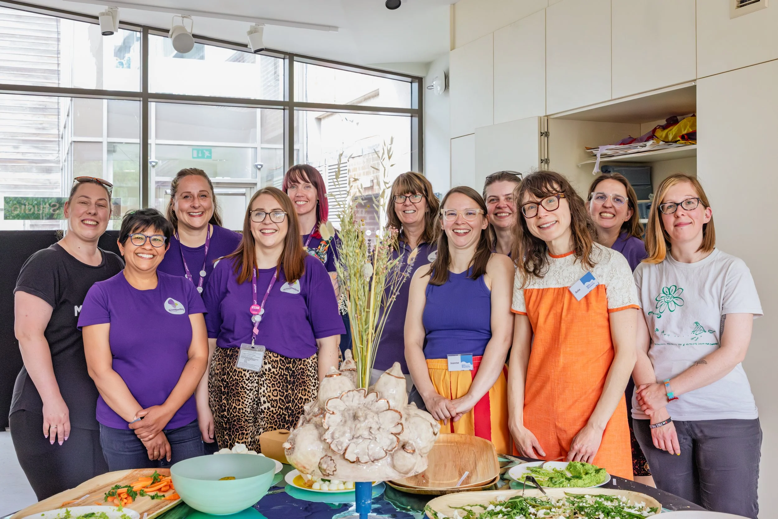 A group of women smiling for the camera standing behind a buffet.
