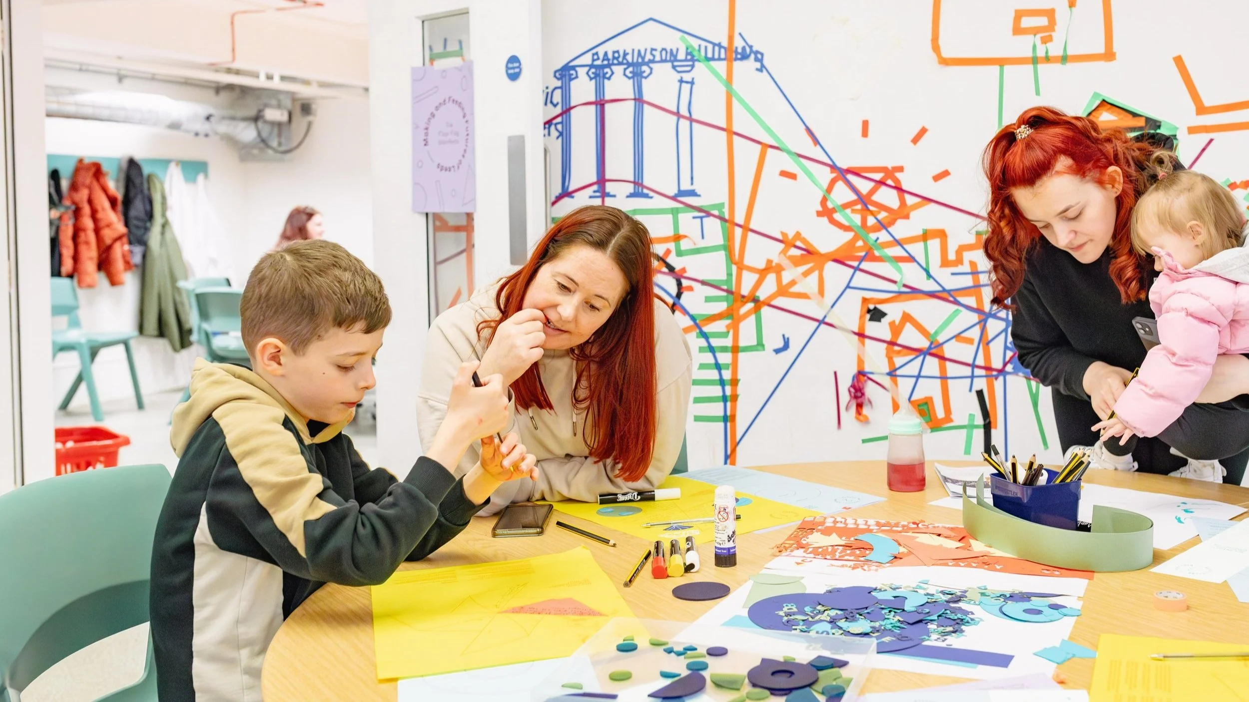 A group of woman and children, looking at colourful worksheets on a table.