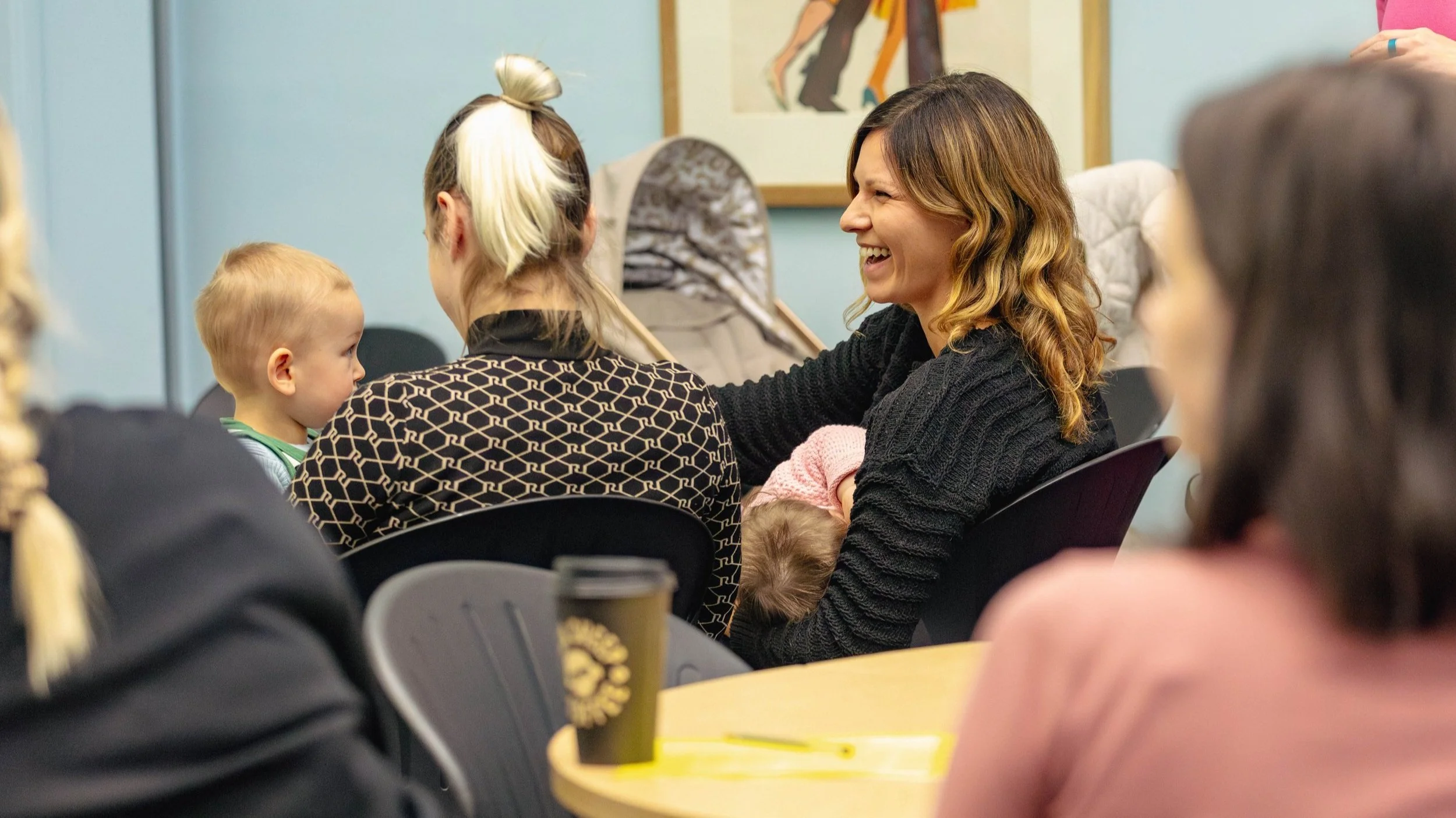 A group of people sitting in a conference room. One person is breastfeeding a baby.
