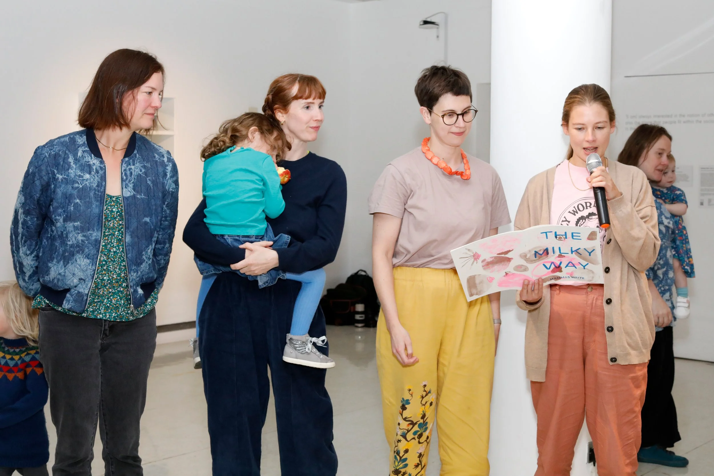 Four women standing in a line; one carries a small child and another holds a zine booklet.