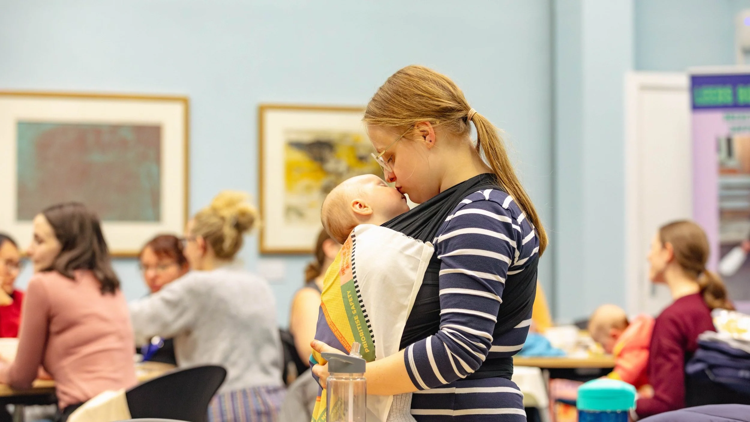 A woman kissing her baby, which she carries in a sling.