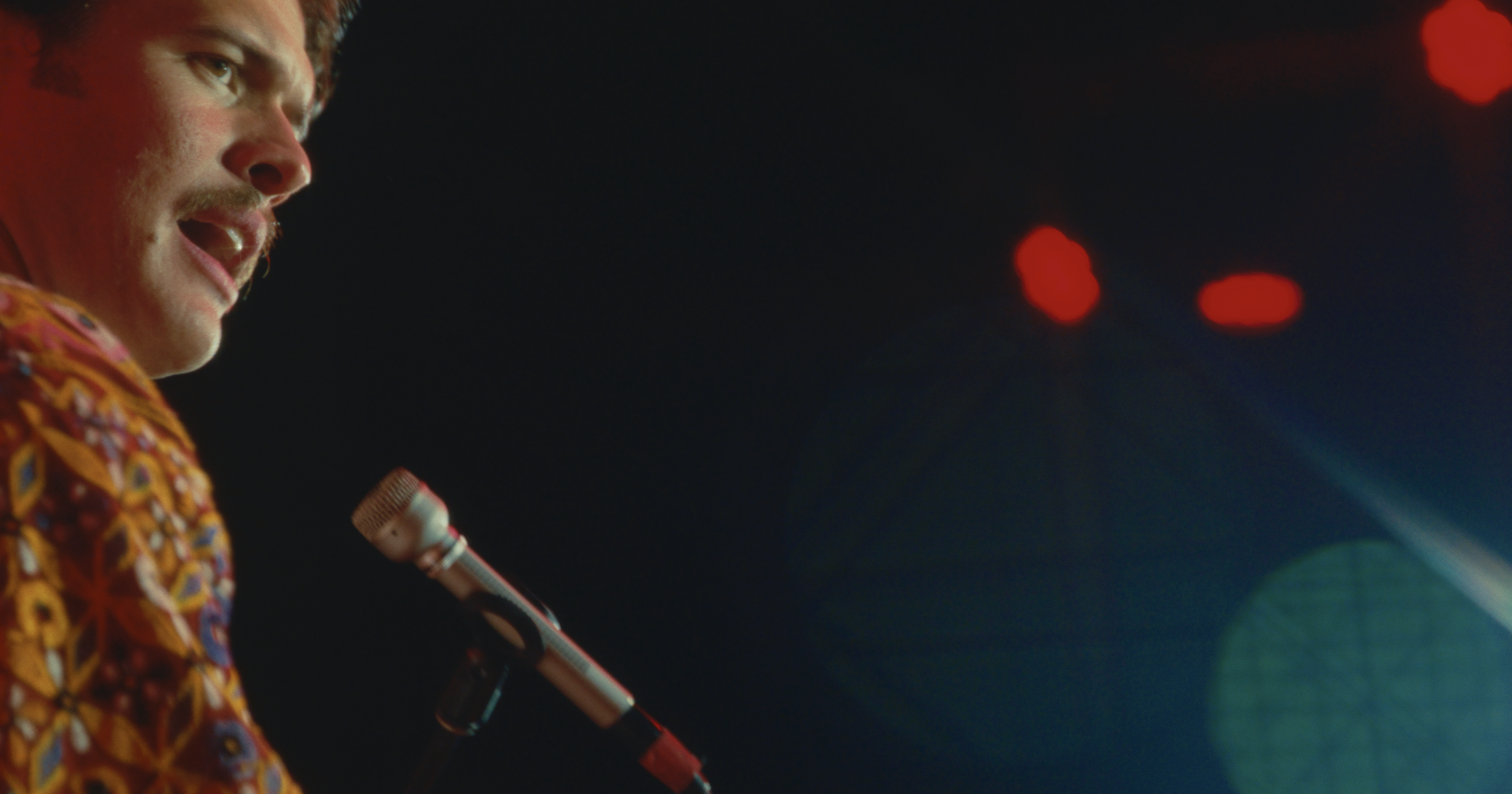 Joe May singing into a microphone on stage with colorful lights.