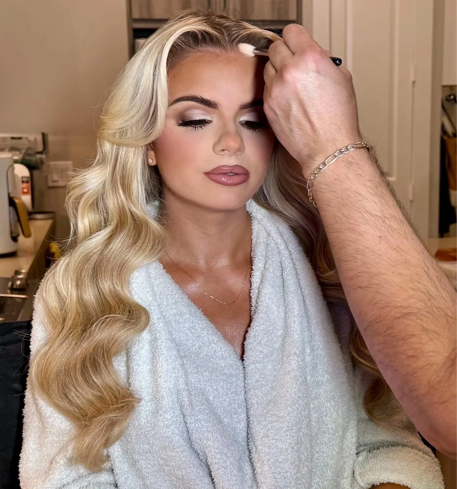 Bride in a white lace wedding dress holding a bouquet of pink, orange, and white flowers outdoors near a pool and greenery at sunset.