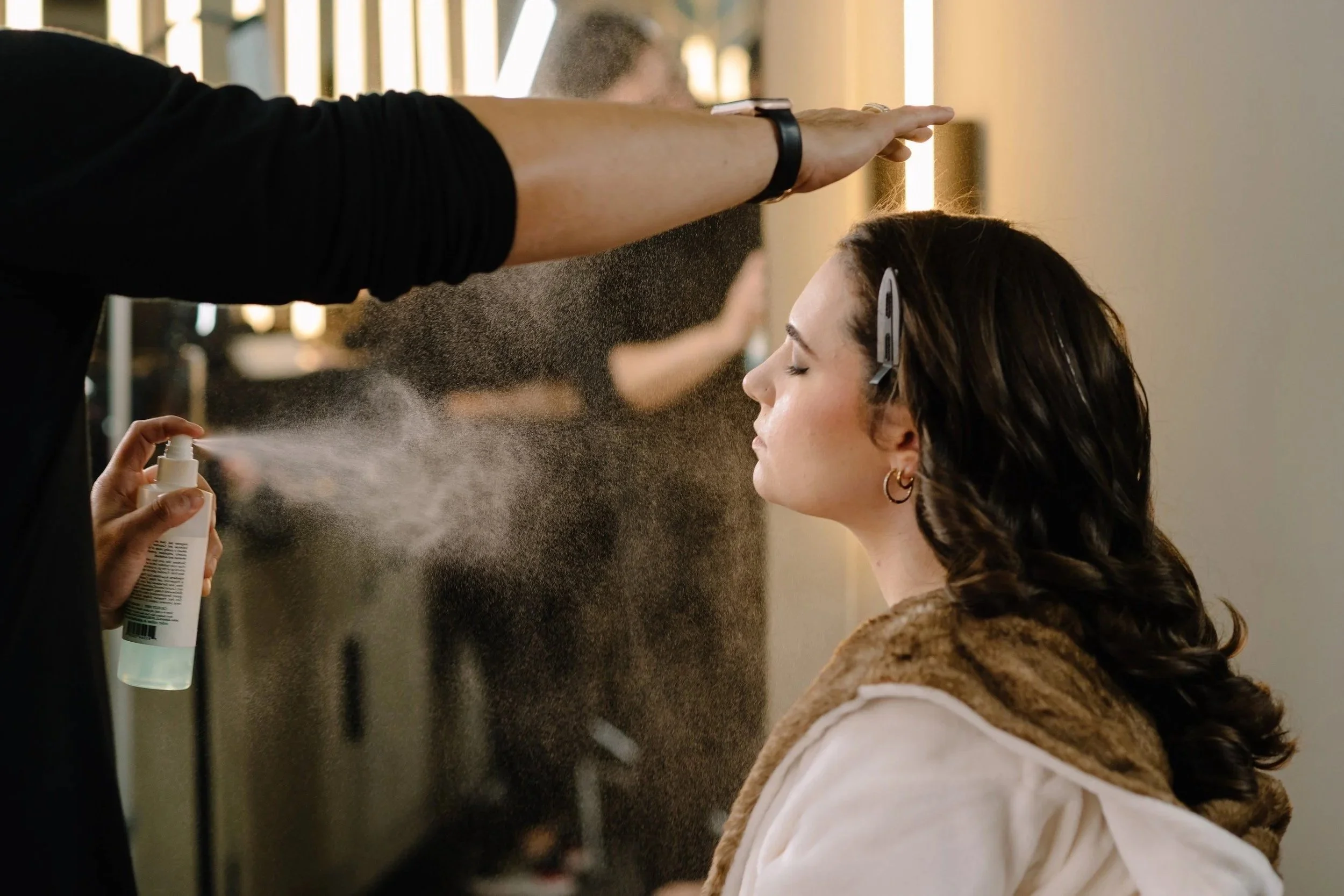 Bride in a white lace wedding dress holding a bouquet of pink, orange, and white flowers outdoors near a pool and greenery at sunset.