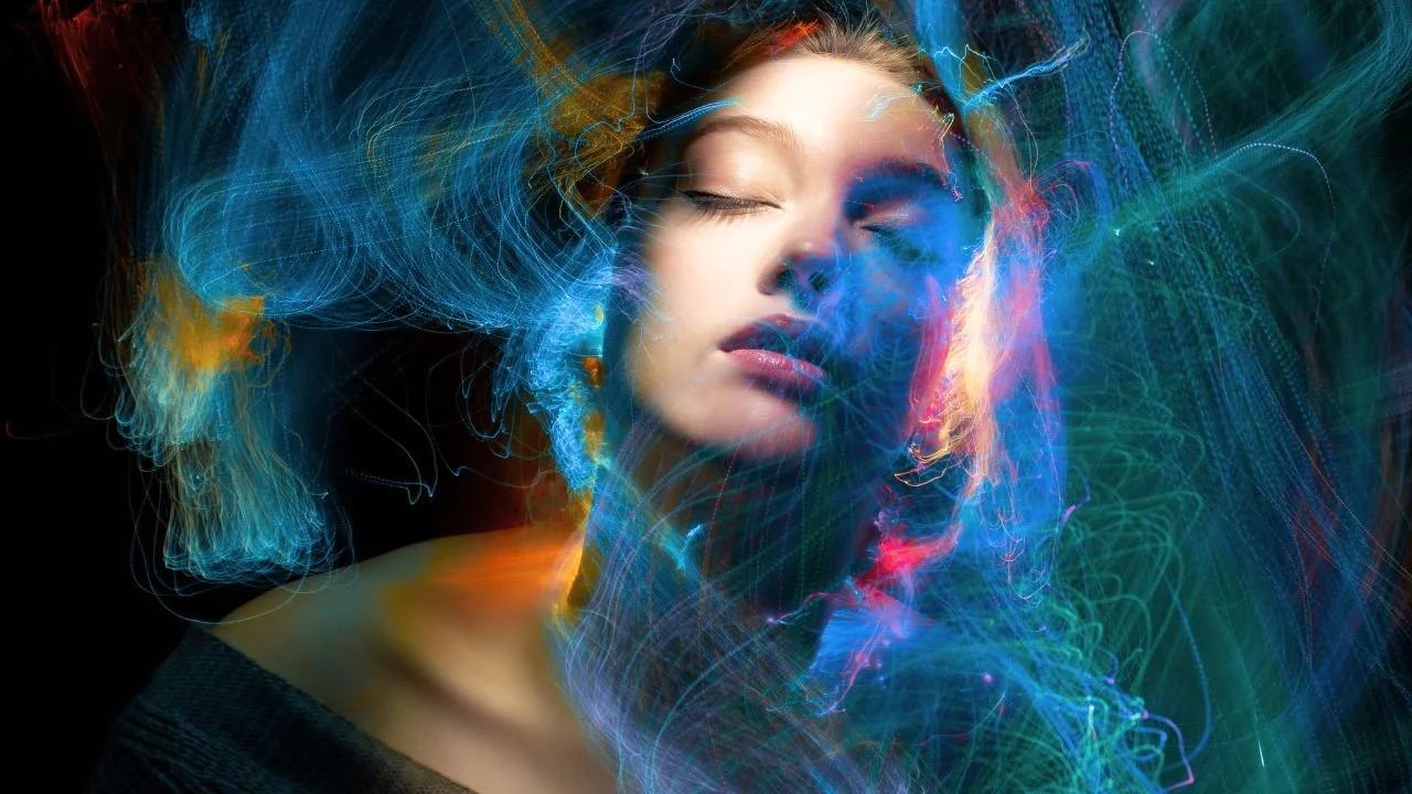 A woman with closed eyes surrounded by swirling, colorful light trails.