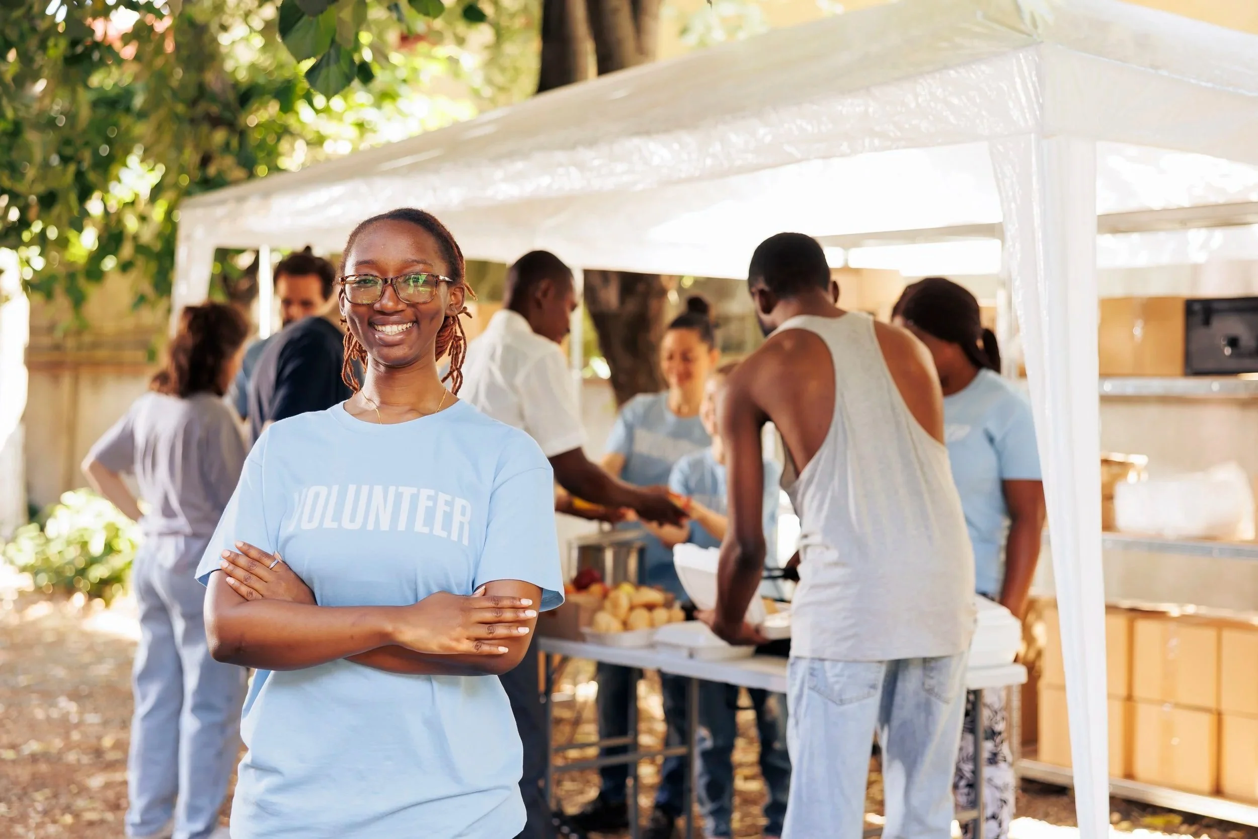 young-black-woman-with-glasses-stands-outdoors-arms-crossed-looking-camera-diverse-group-volunteers-supports-non-profit-program-dedicated-hunger-relief-helping-needy-individuals.jpg