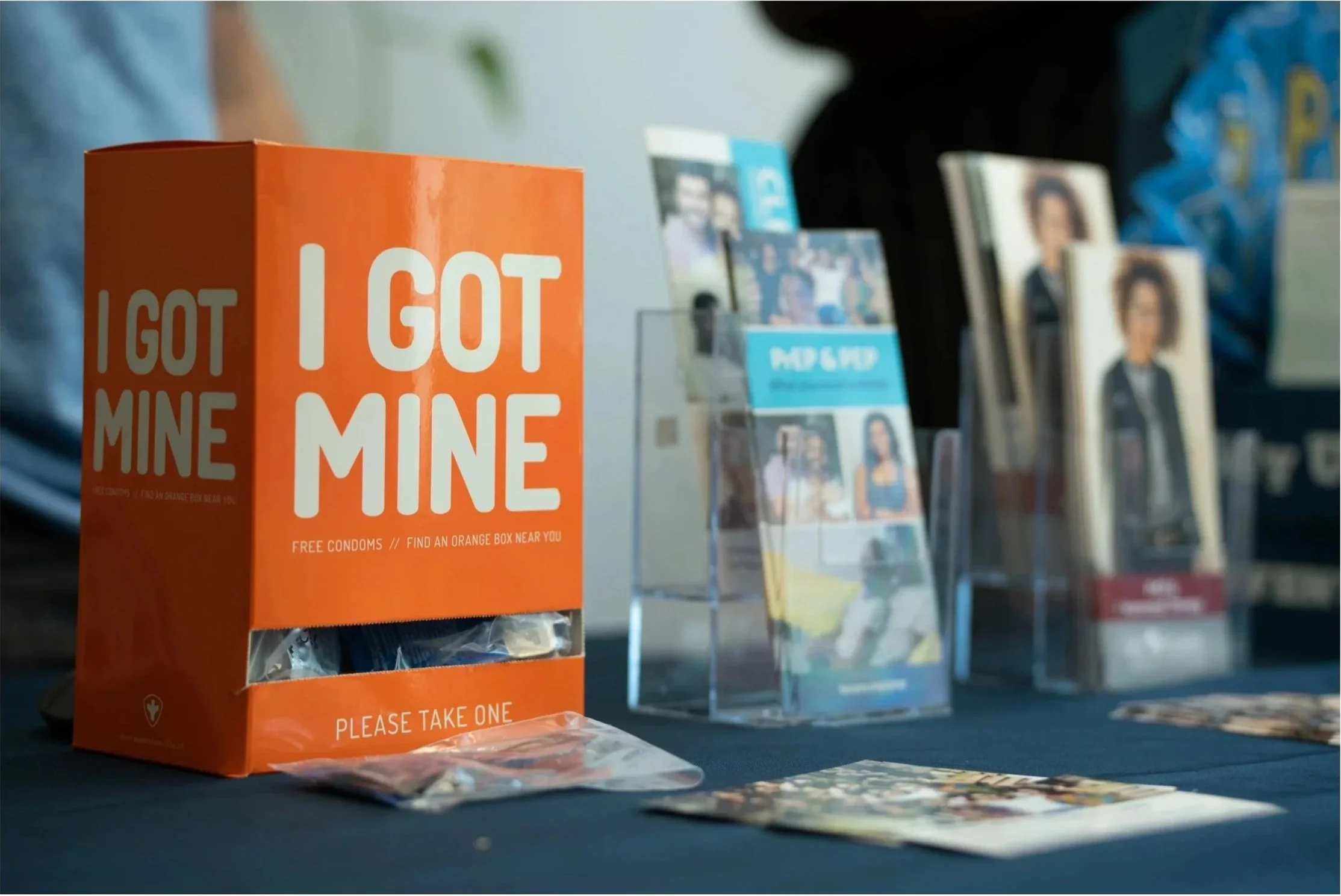 An orange box with the text 'I GOT MINE' contains free condoms, placed on a table at an event.