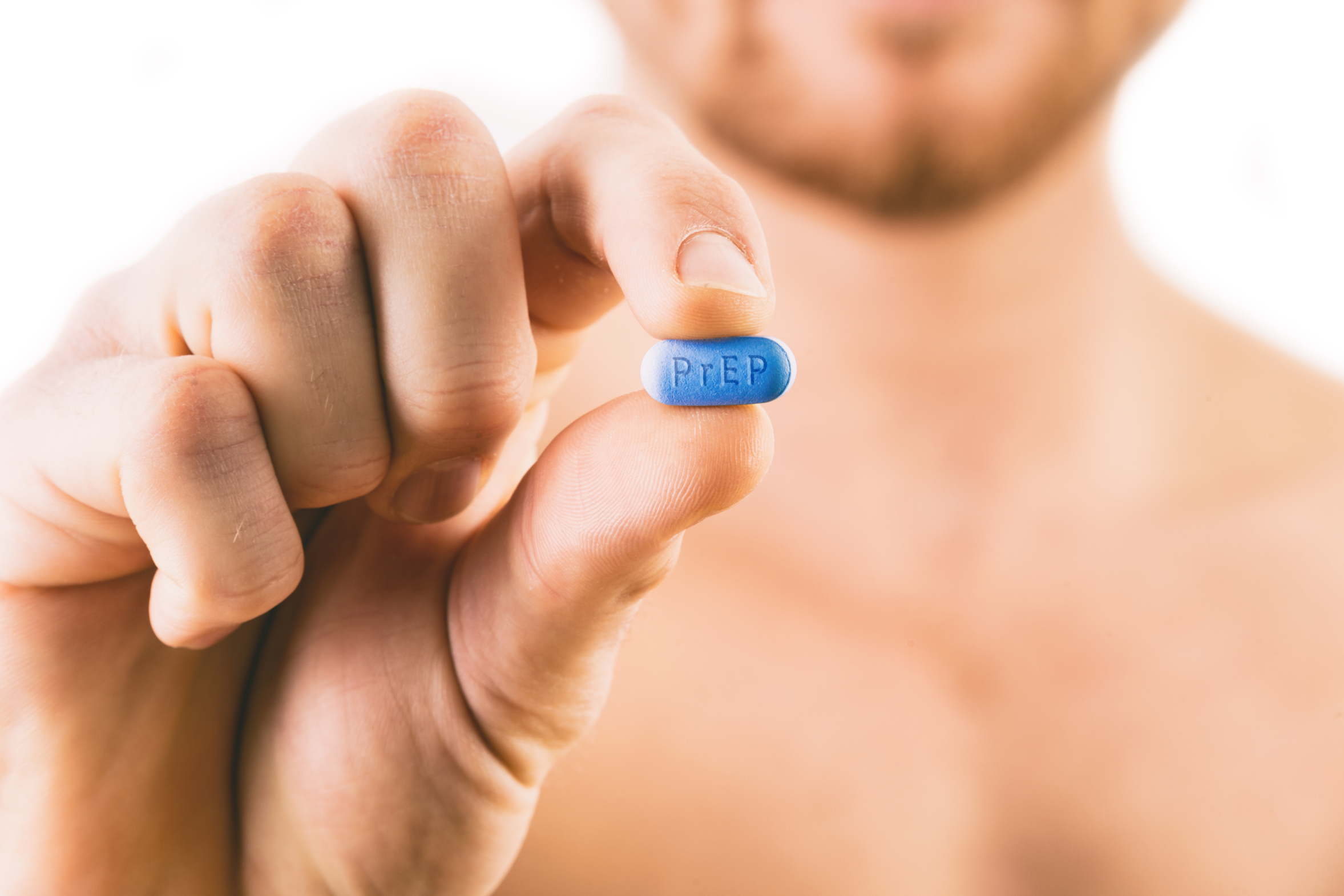 A person holding a blue pill with the word 'PREP' written on it in front of a blurred background.