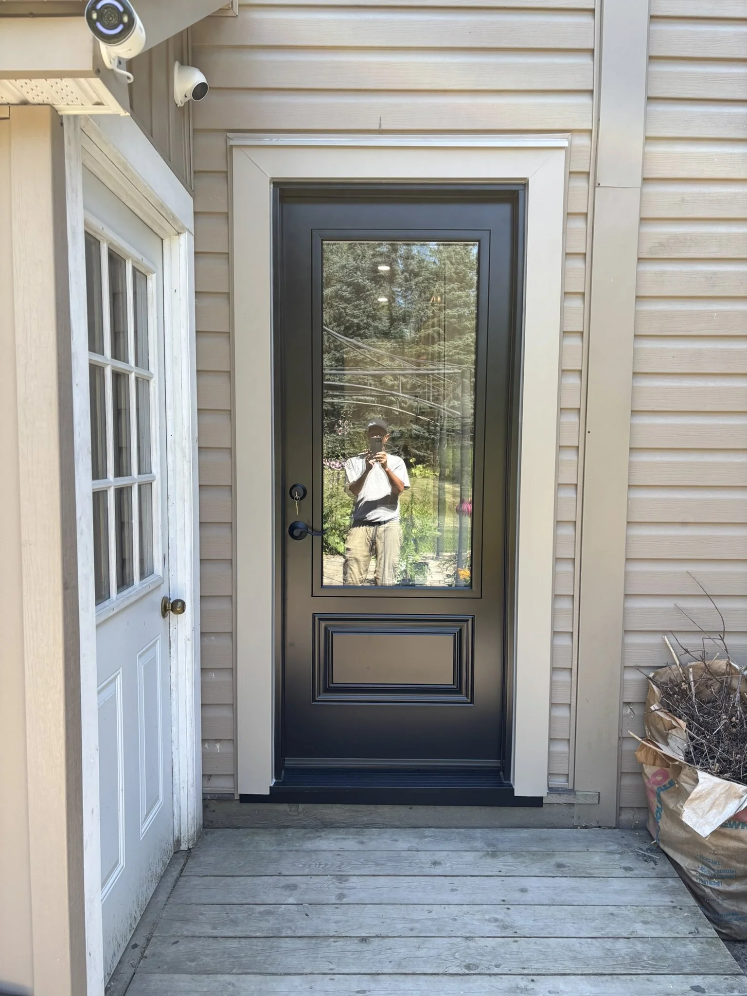 Reflected image of a person taking a photo in a glass door, with trees and outdoor scenery in the background.