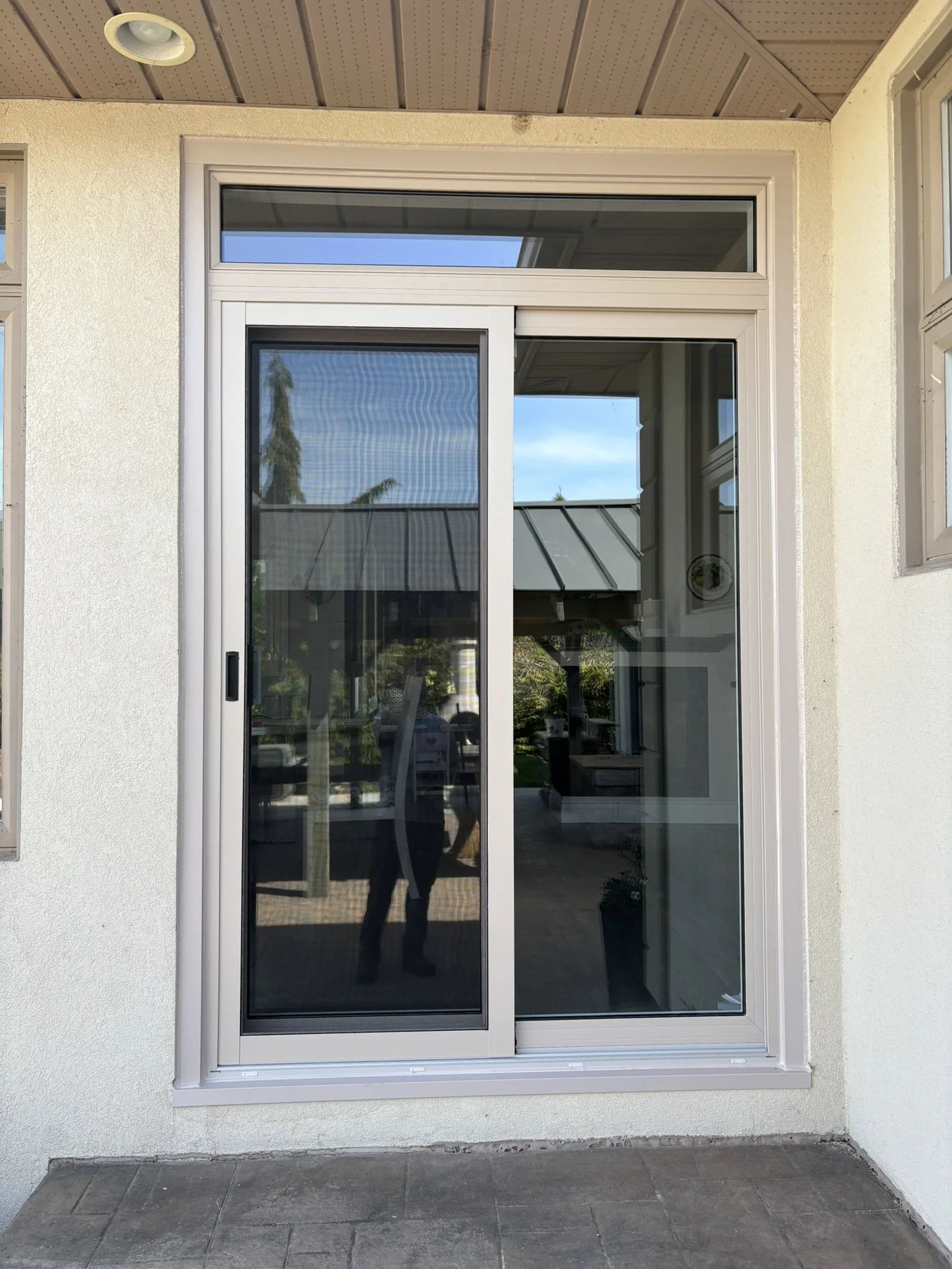 A sliding glass door with a white frame leading into a house, with a partial view of the interior and reflections of trees and the sky on the glass.