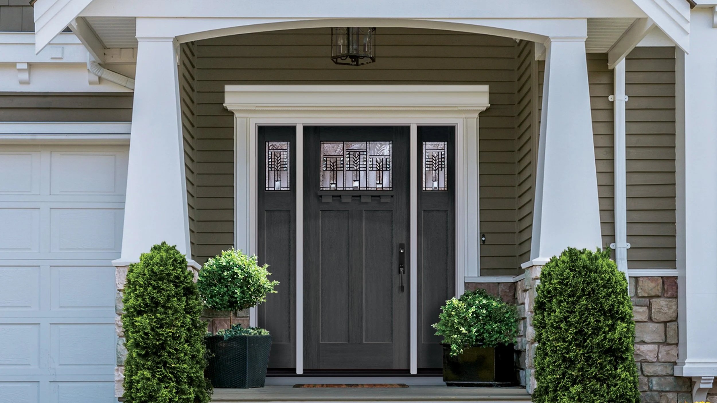 The image depicts the front door area of a house with a black door featuring decorative glass panels. The house has beige horizontal siding, white trim, and two small bushes on either side of the door. There is a porch ceiling with a hanging lantern-style light.