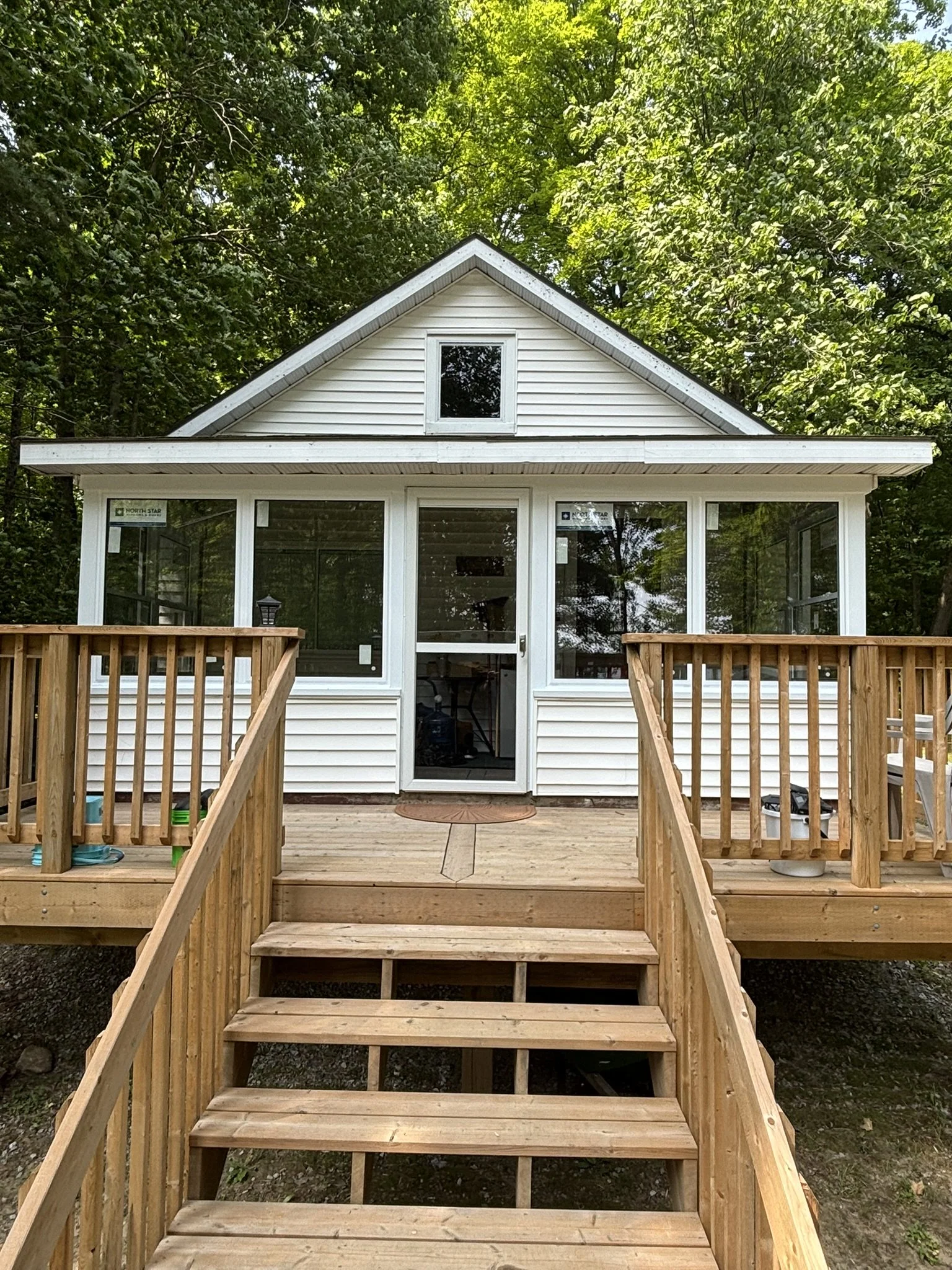 A house with white siding and a screened porch, wooden stairs leading up to the porch, surrounded by green trees.