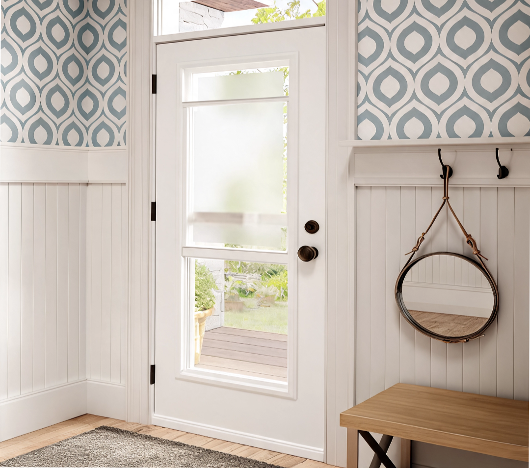 White door with glass panel leading to a porch with greenery outside, blue patterned wallpaper, a small mirror hanging from hooks, and a wooden bench inside.