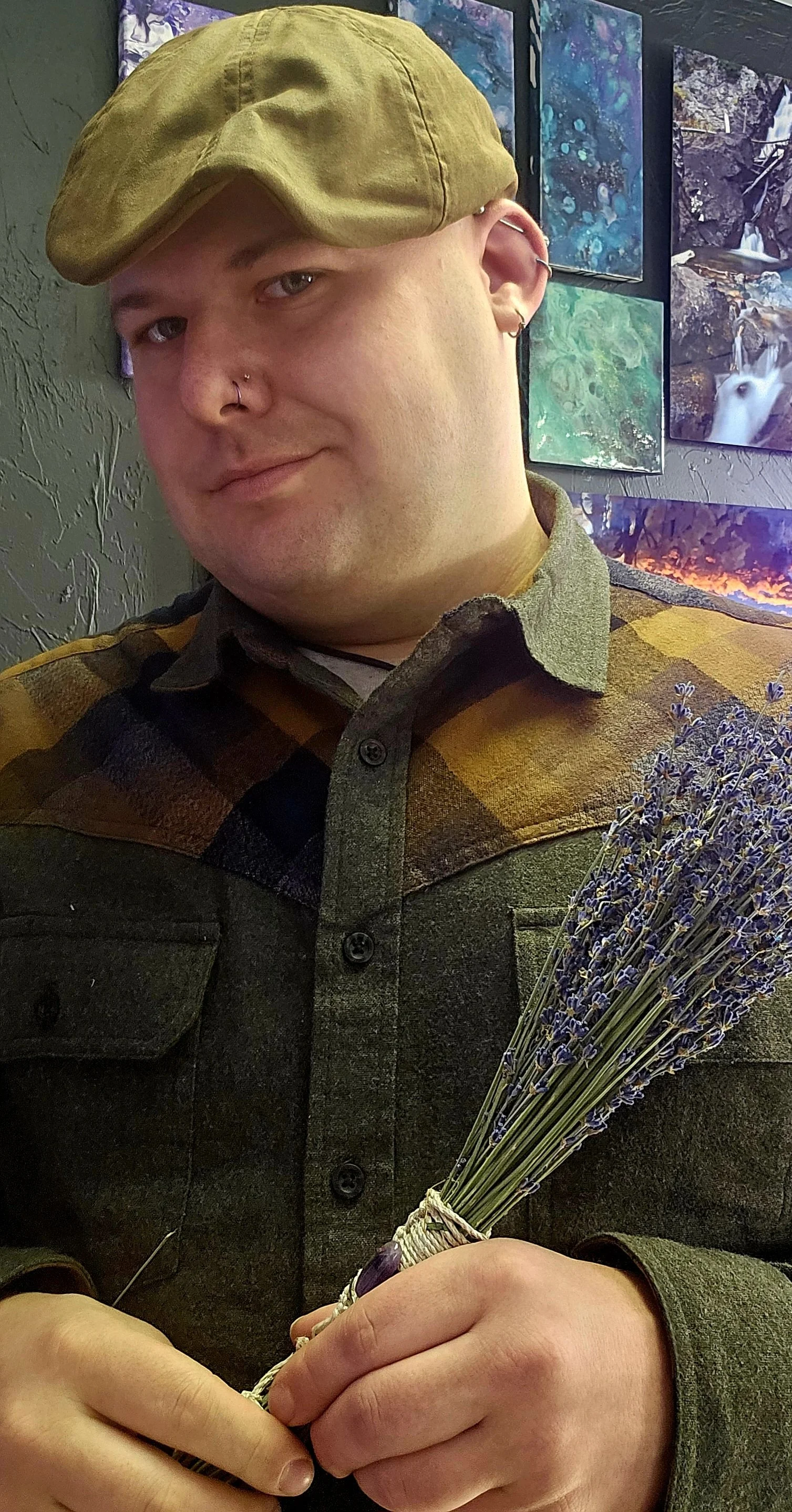 A man wearing a green hat and a plaid shirt holding a bouquet of lavender flowers.