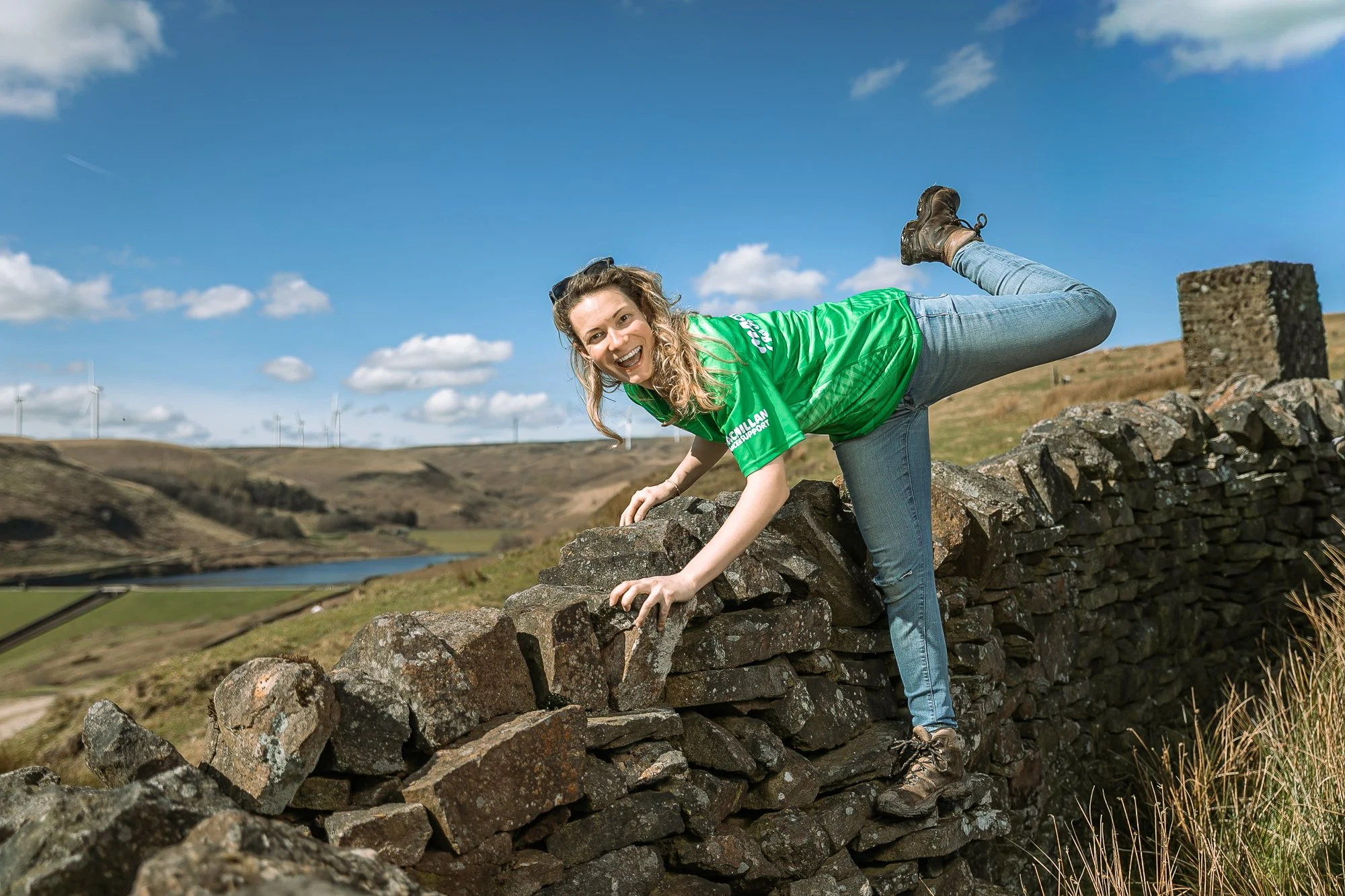 Roxane in green Macmillan t-shirt hiking and balancing on a stone wall in the countryside during marathon training