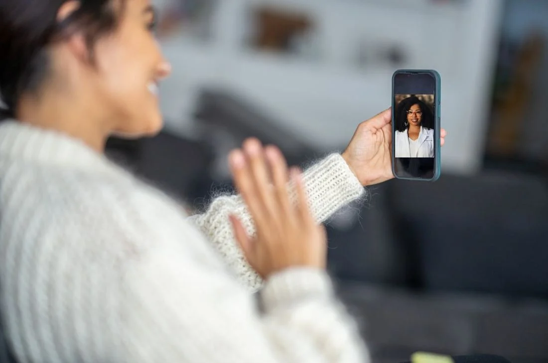 A smiling patient waves to Dr. Richmond during a video appointment on her phone