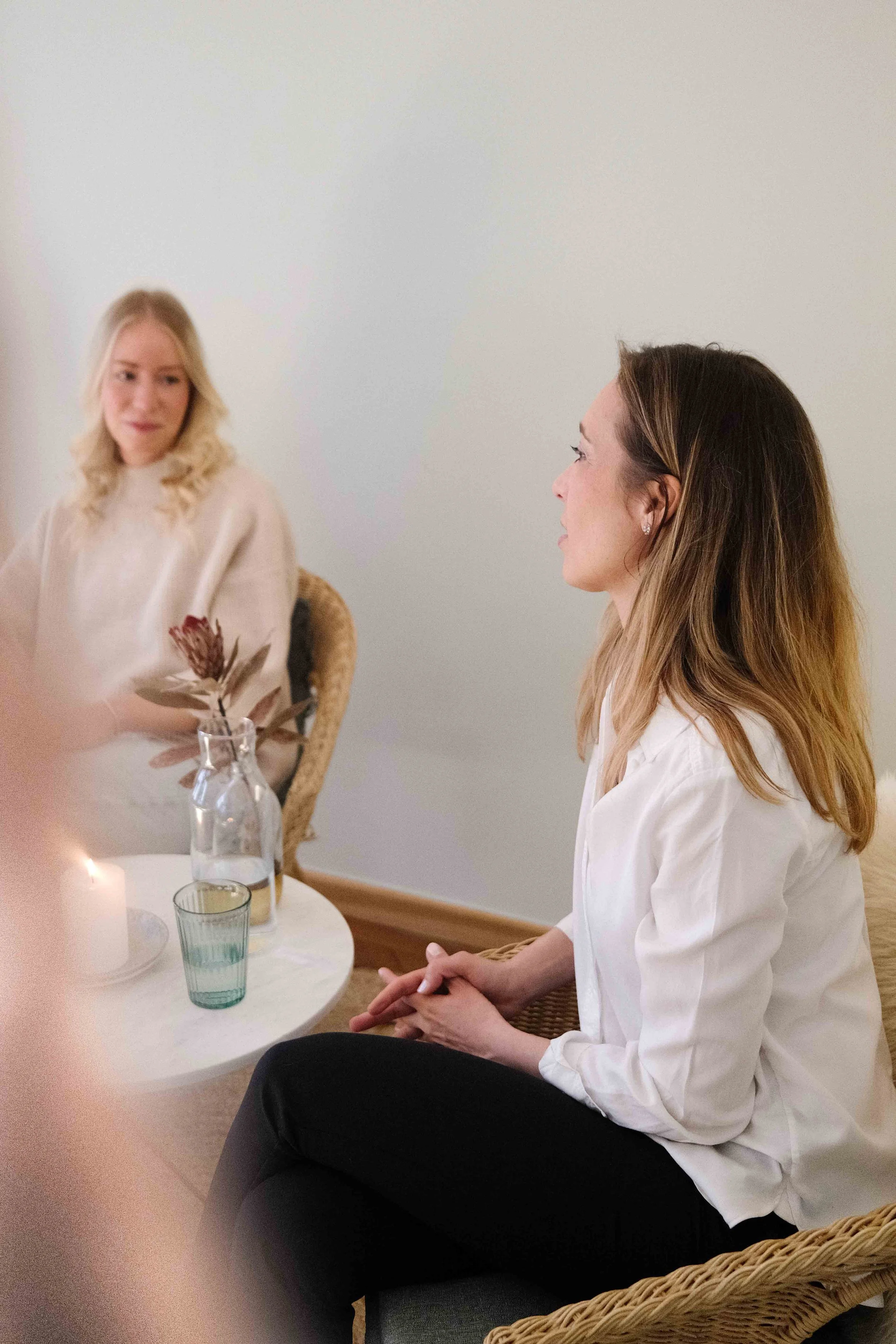 Nicole im Gespräch in einem ruhigen Coaching-Setting. Zwei Stühle, eine Blume in einer Vase, eine Kerze, warme Atmosphäre.