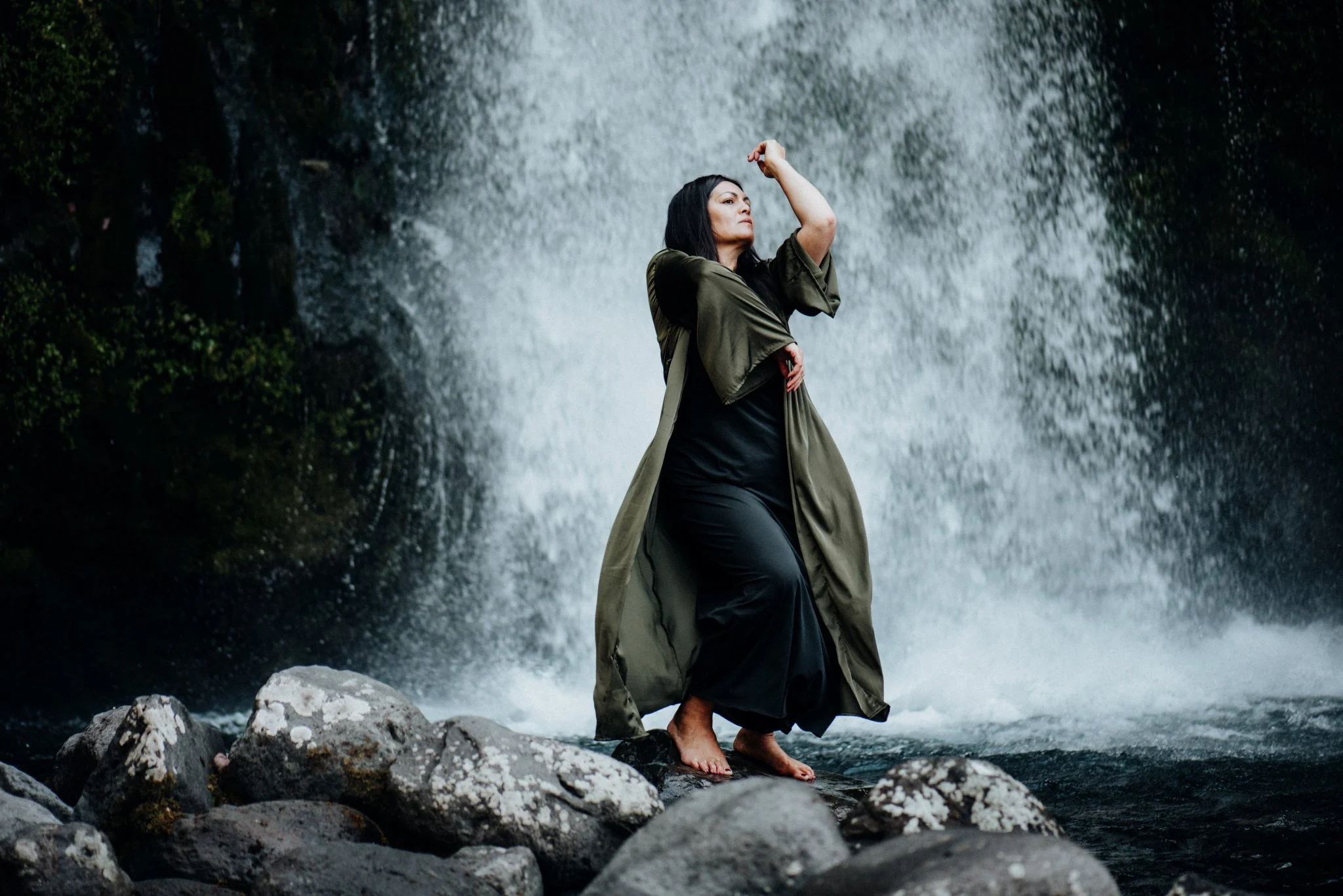 A woman sitting in a grassy field with her eyes closed, enjoying the outdoor scenery on a cloudy day.