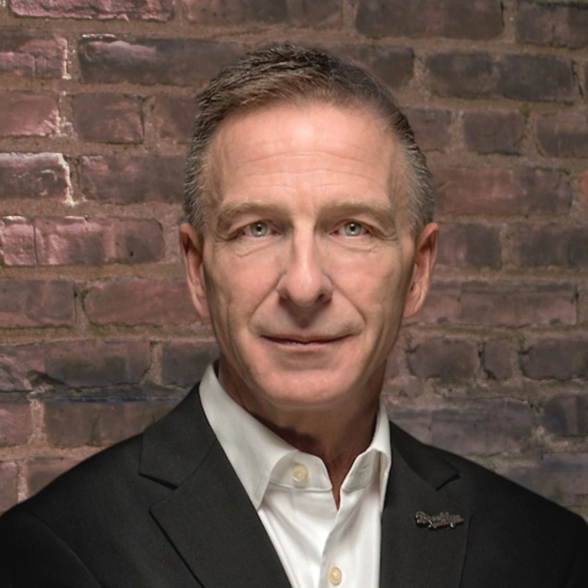 Portrait of a man in a suit against a brick wall background.
