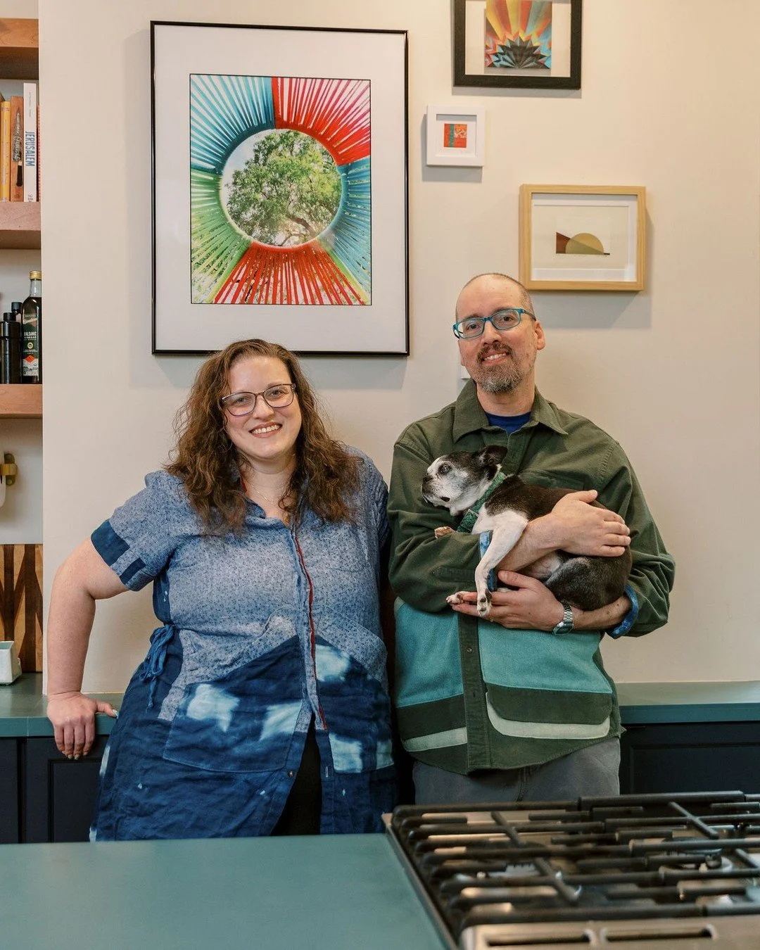 Human artists, with a perfect little princess (not robot) dog, wearing human artist made clothing in front of human made art, in a kitchen designed and built by humans. 

Representing their small business dedicated to supporting handmade artists and 