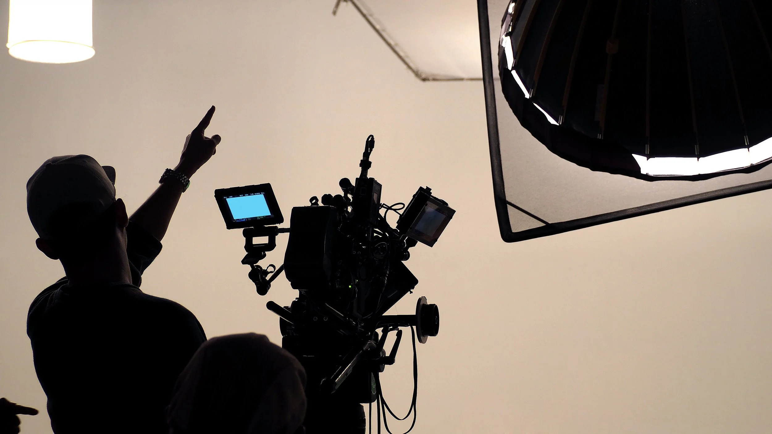 Silhouetted person with a cap pointing upward in a photography studio with professional lighting equipment and a camera.