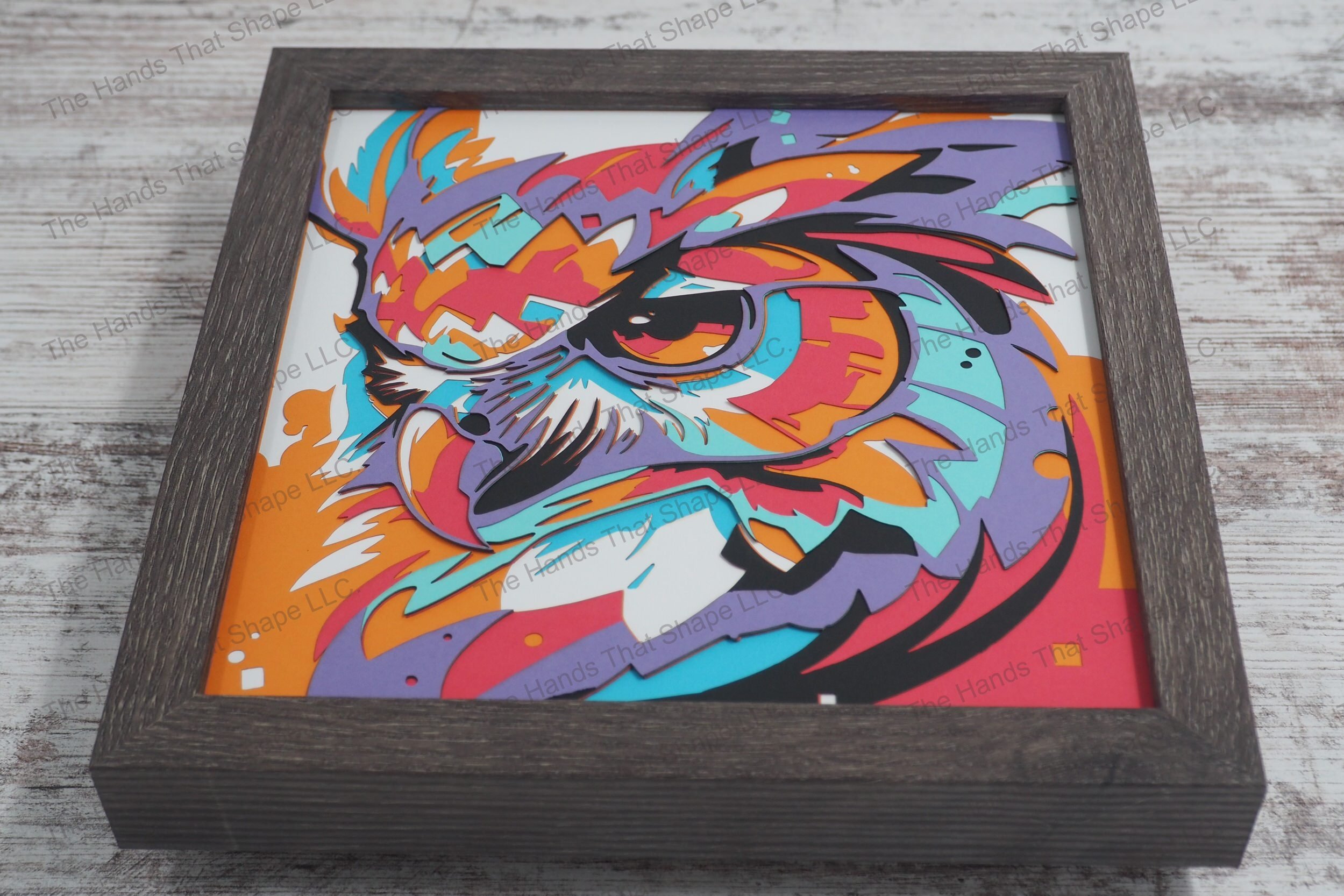 A vibrant layered paper shadowbox depicting the head of an owl in vivid colors, crafted from 7 layers of cardstock, encased in a gray MDF frame.