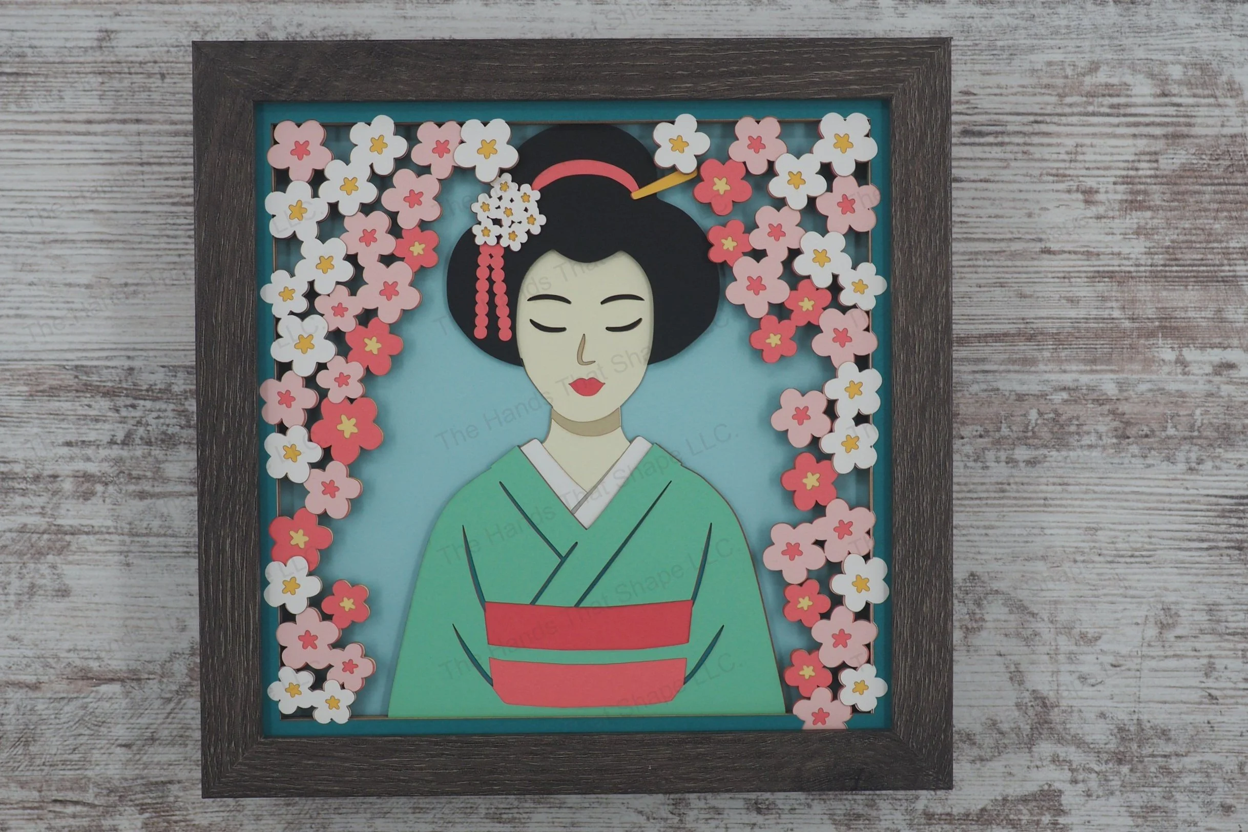 A graceful 3D layered paper shadowbox featuring a traditionally dressed geisha surrounded by falling cherry blossoms and intricate floral hair ornaments.
