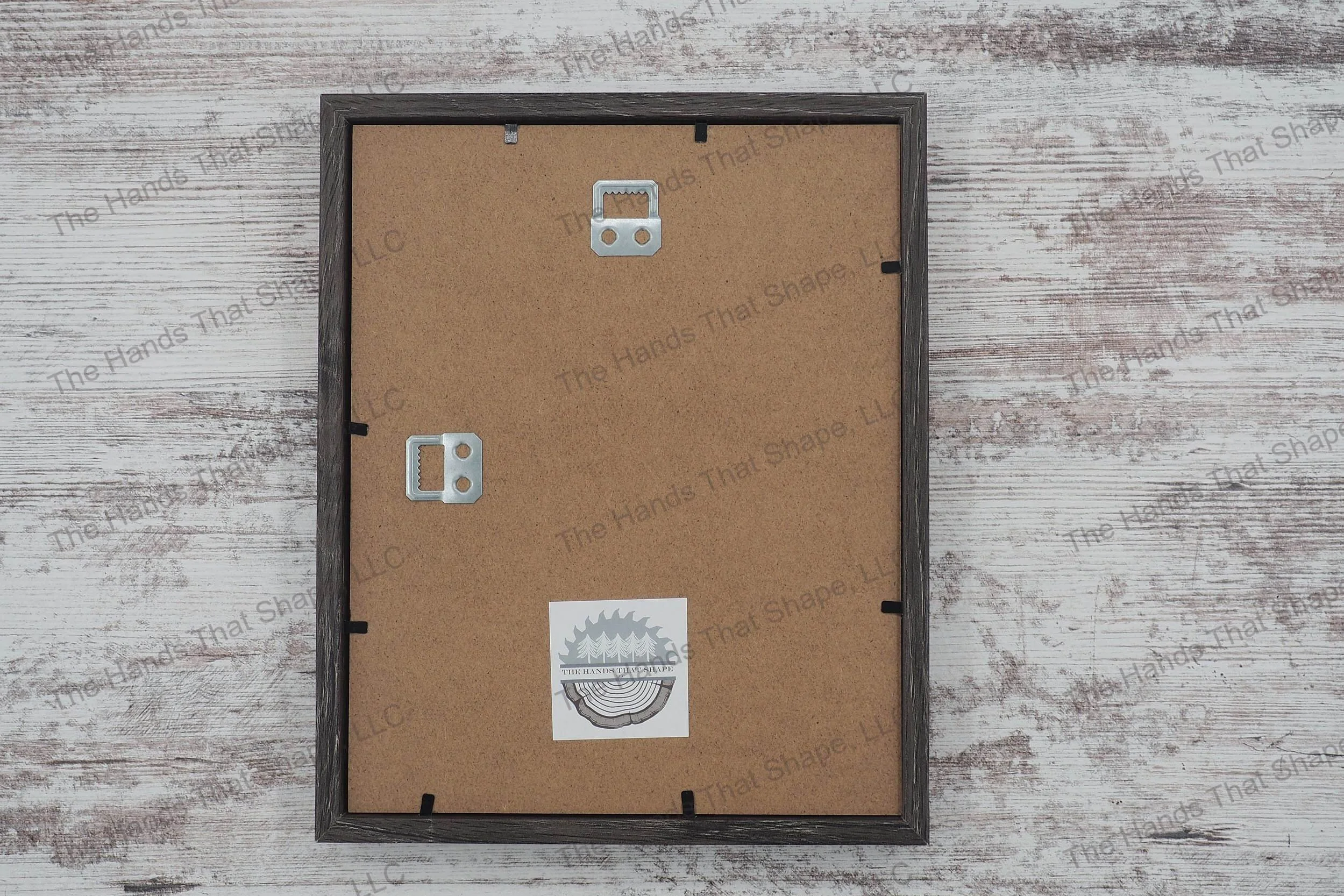 The back side of the layered cardstock paper shadow box that uses sheets of paper to create a 3d image. The backside shows The Hands That Shape, LLC logo and mounted hanger.