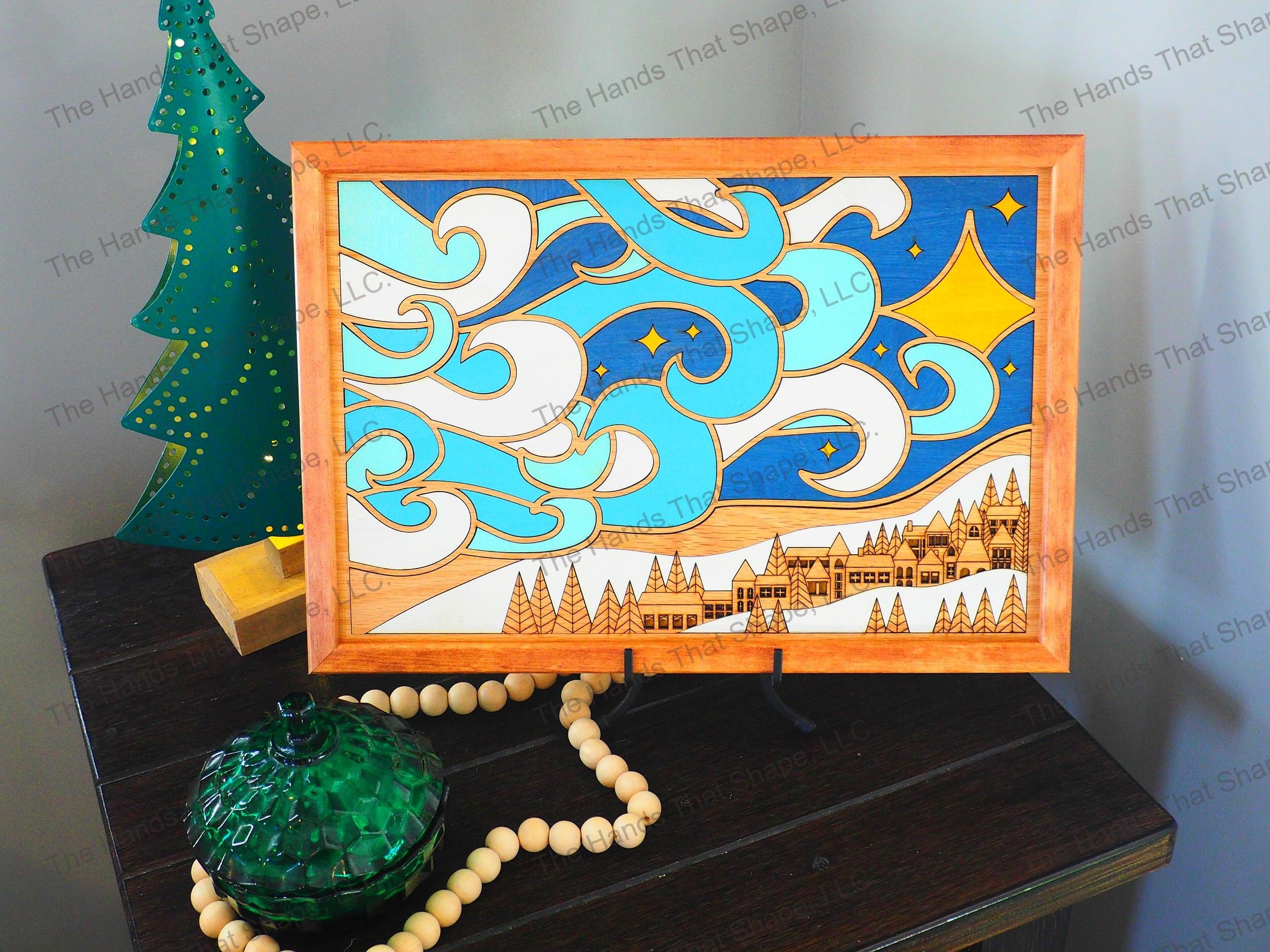The “Winter Village” wood wall art features a beautiful village below swirling wind and a vibrant blue night sky.