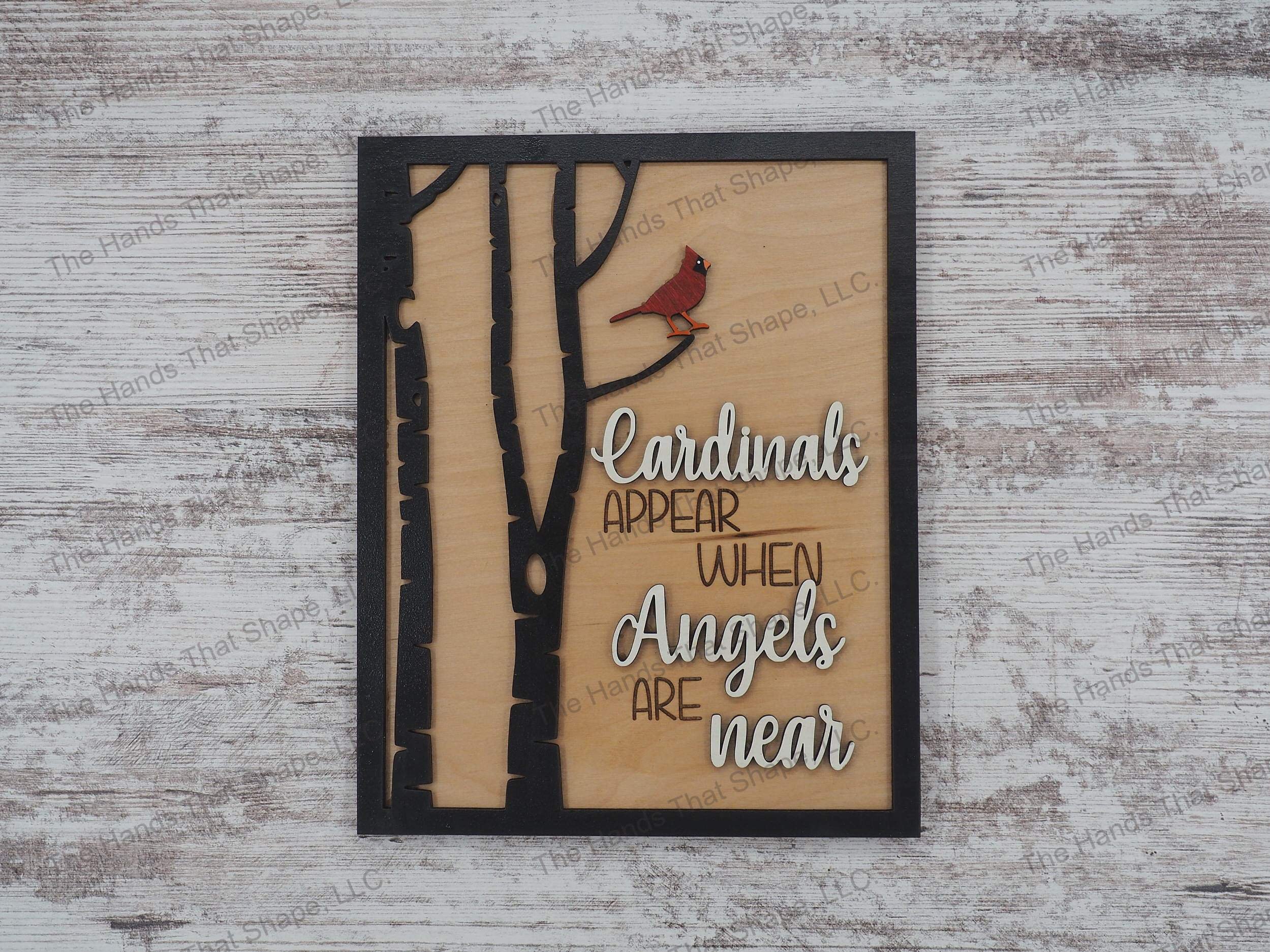 The ”Cardinals Appear” art features a red cardinal perched in a tree with an “when angels are near” saying in white.