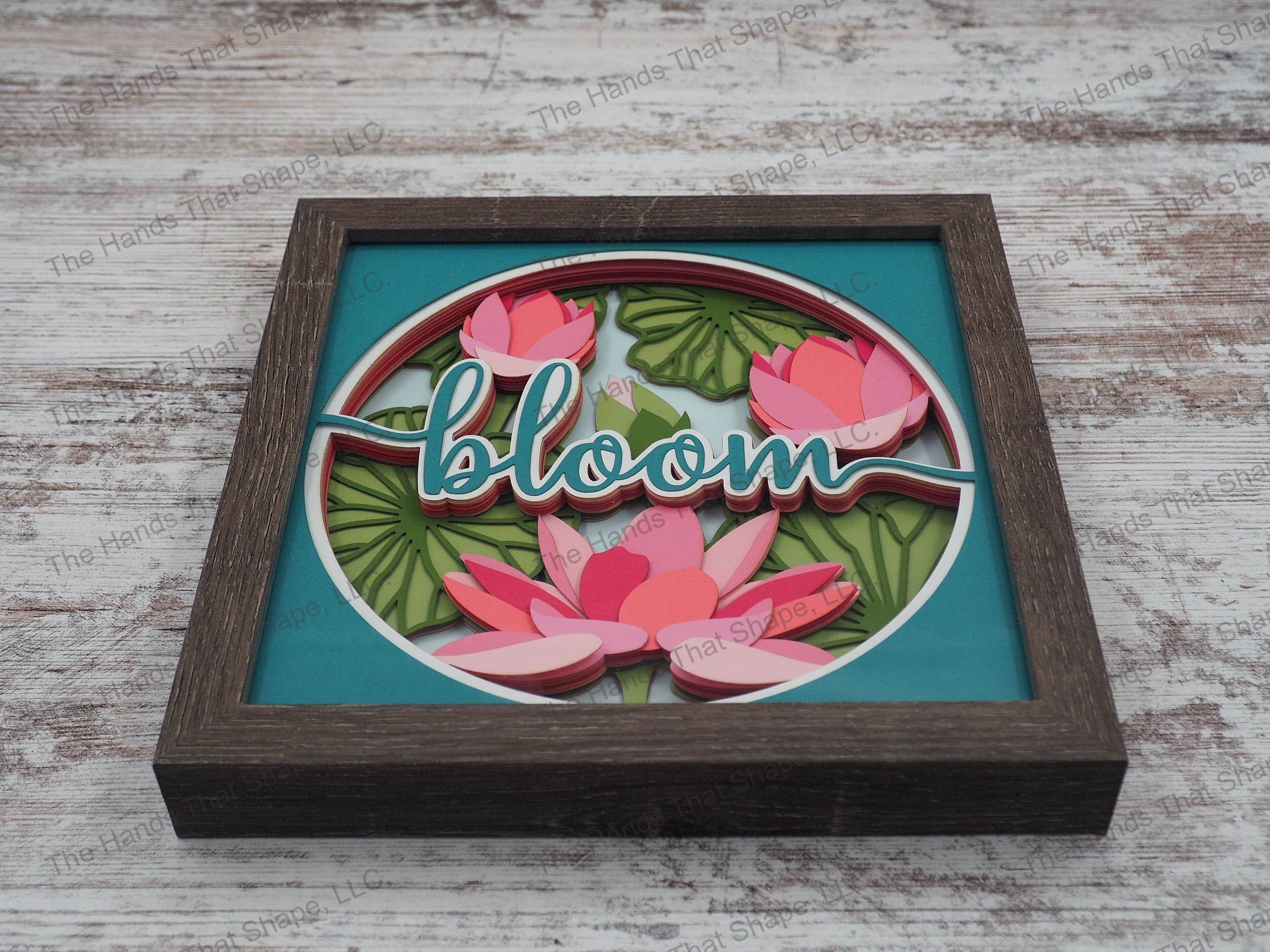 The shadow box features multiple water lilies in the various stages of blooming with the word "BLOOM" in the foreground.