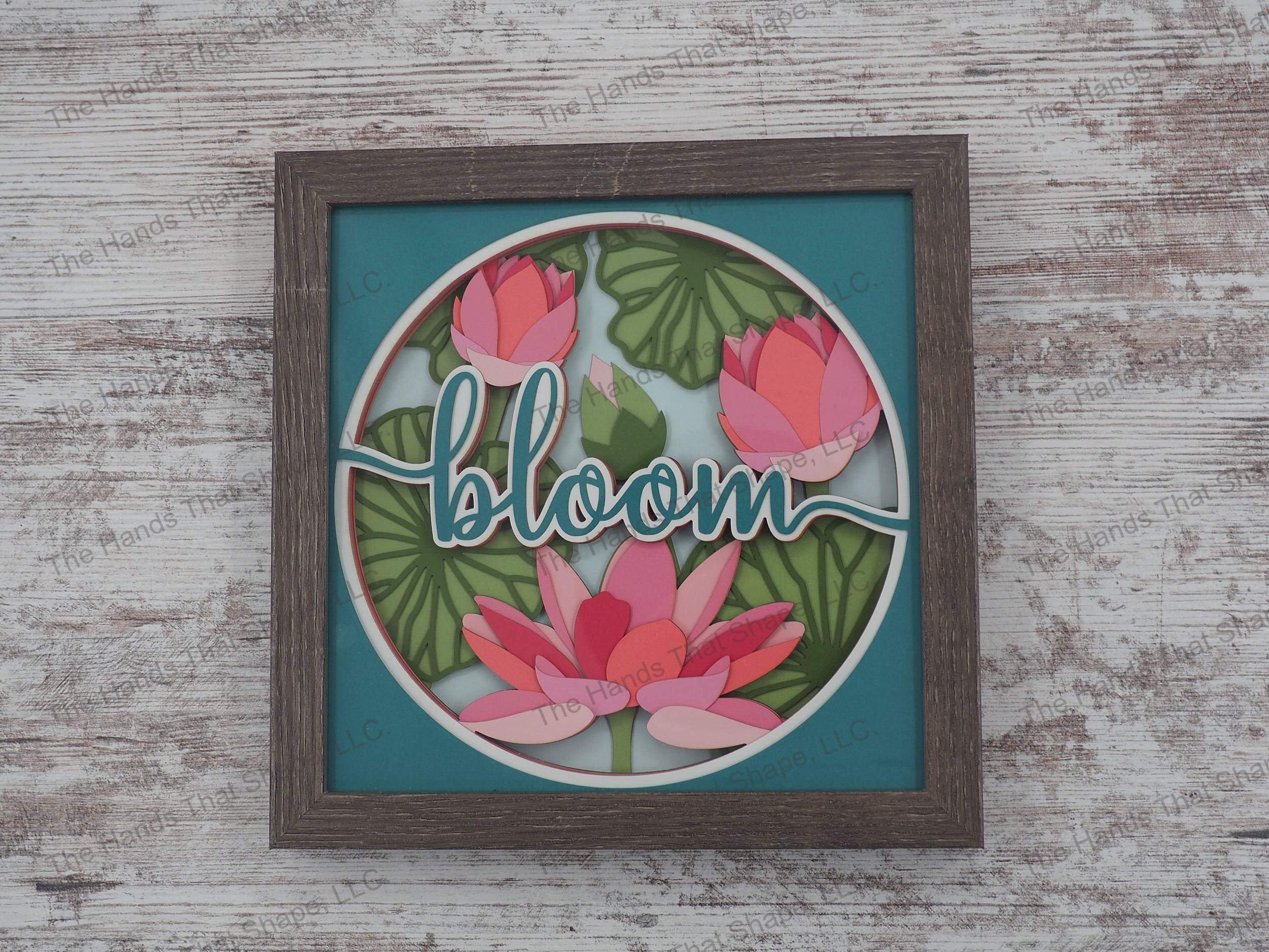The shadow box features multiple water lilies in the various stages of blooming with the word "BLOOM" in the foreground.