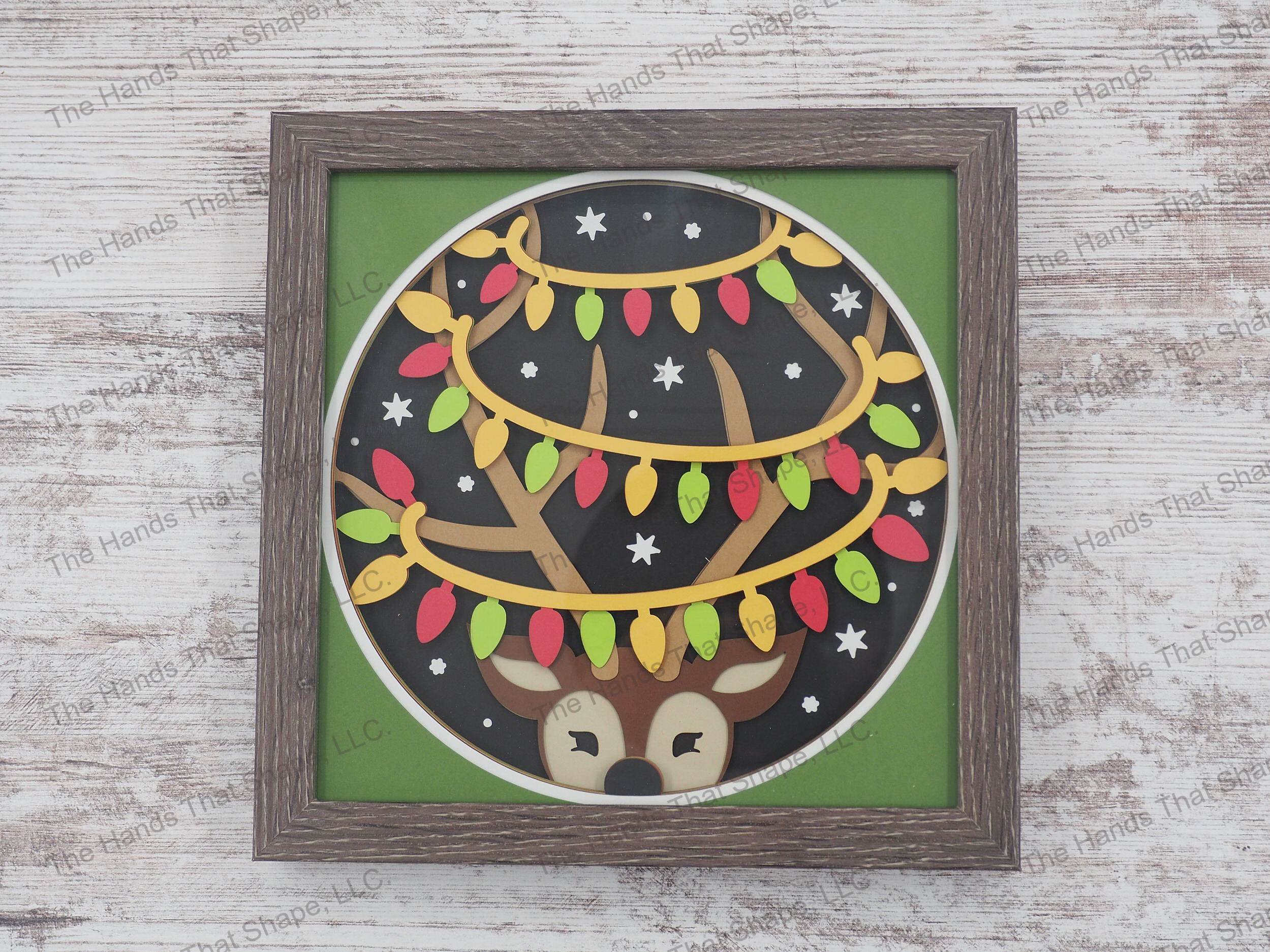 The shadow box features a cute reindeer with it's antlers wrapped in Christmas lights in a playful manner as snow begins to fall.