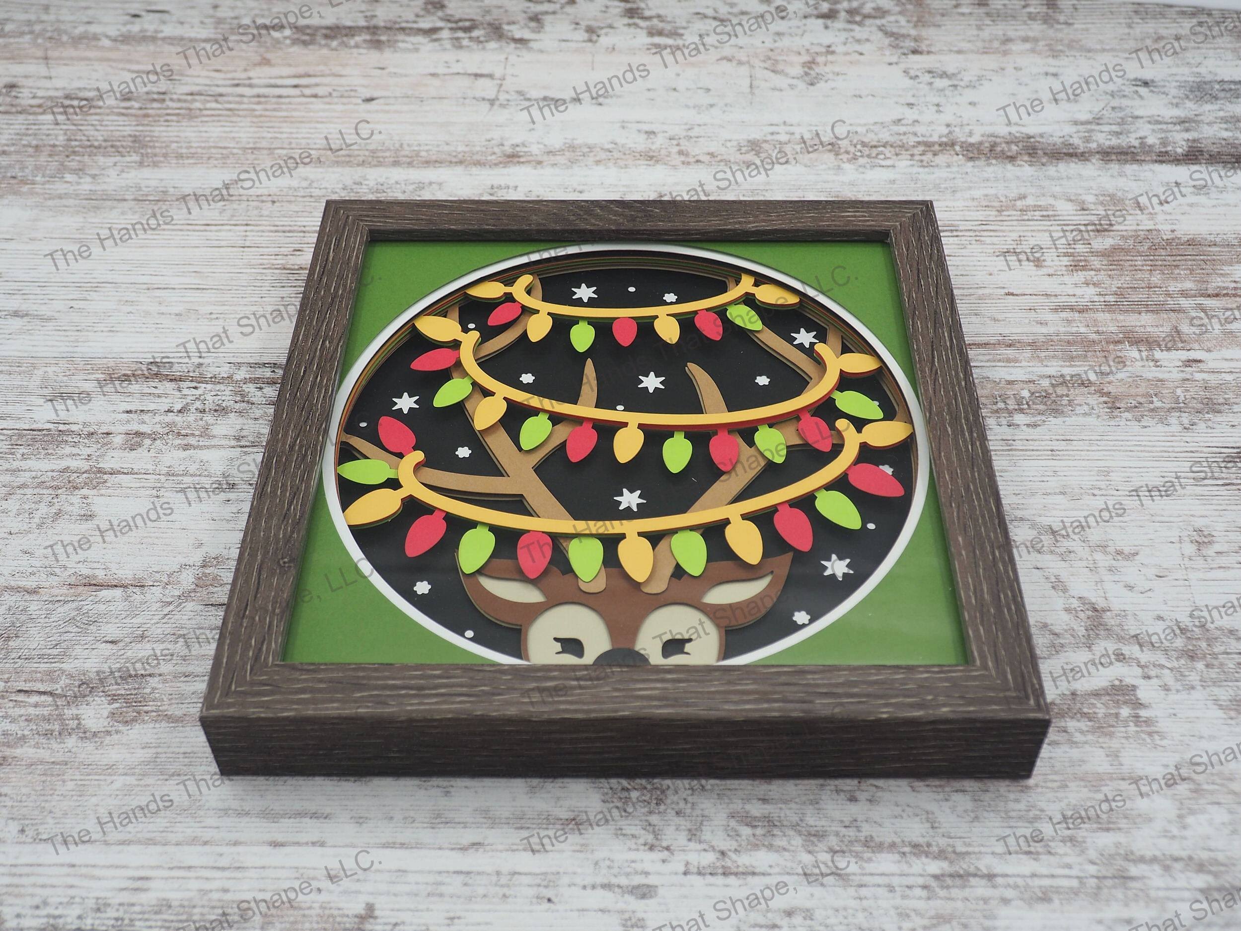 The shadow box features a cute reindeer with it's antlers wrapped in Christmas lights in a playful manner as snow begins to fall.